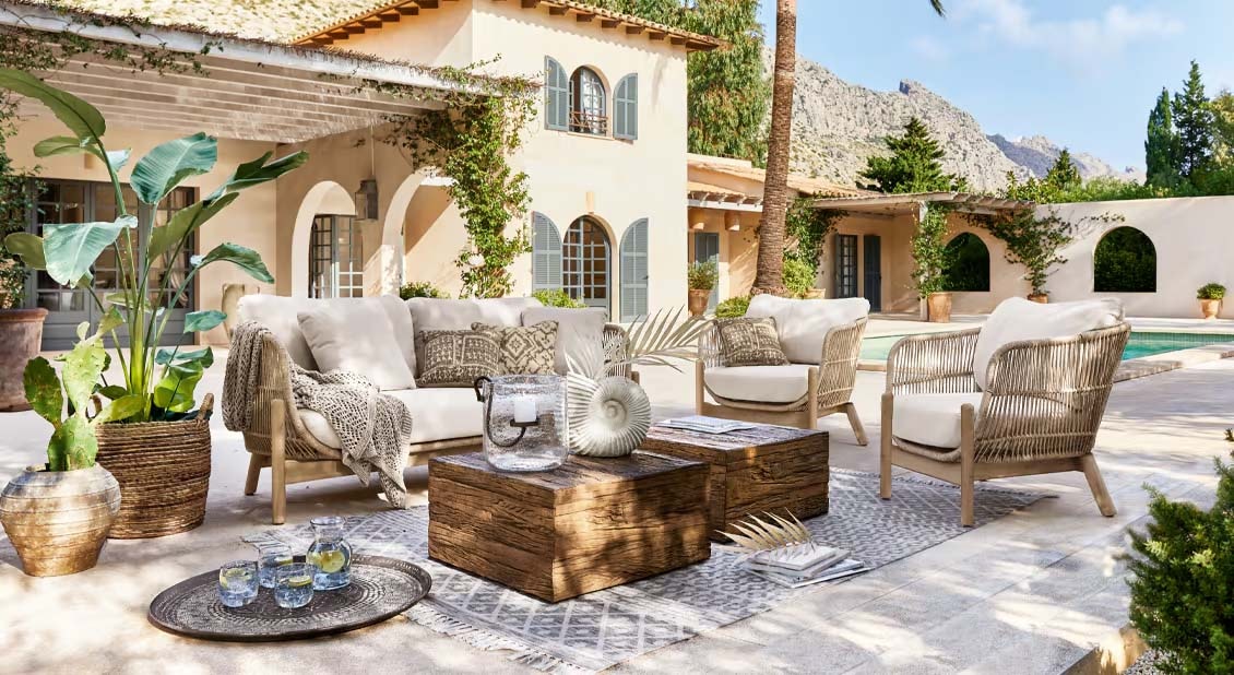 Gartenmöbel-Set mit hellen Polstern und Holztisch auf Terrasse neben Pool in mediterranem Stil