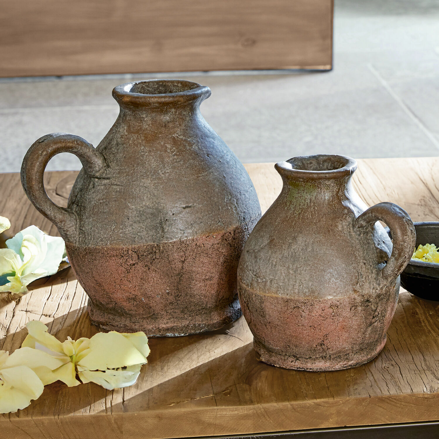 Zwei rustikale Keramikkrüge in braun-roter Farbe auf Holztisch mit Blumen dekoriert