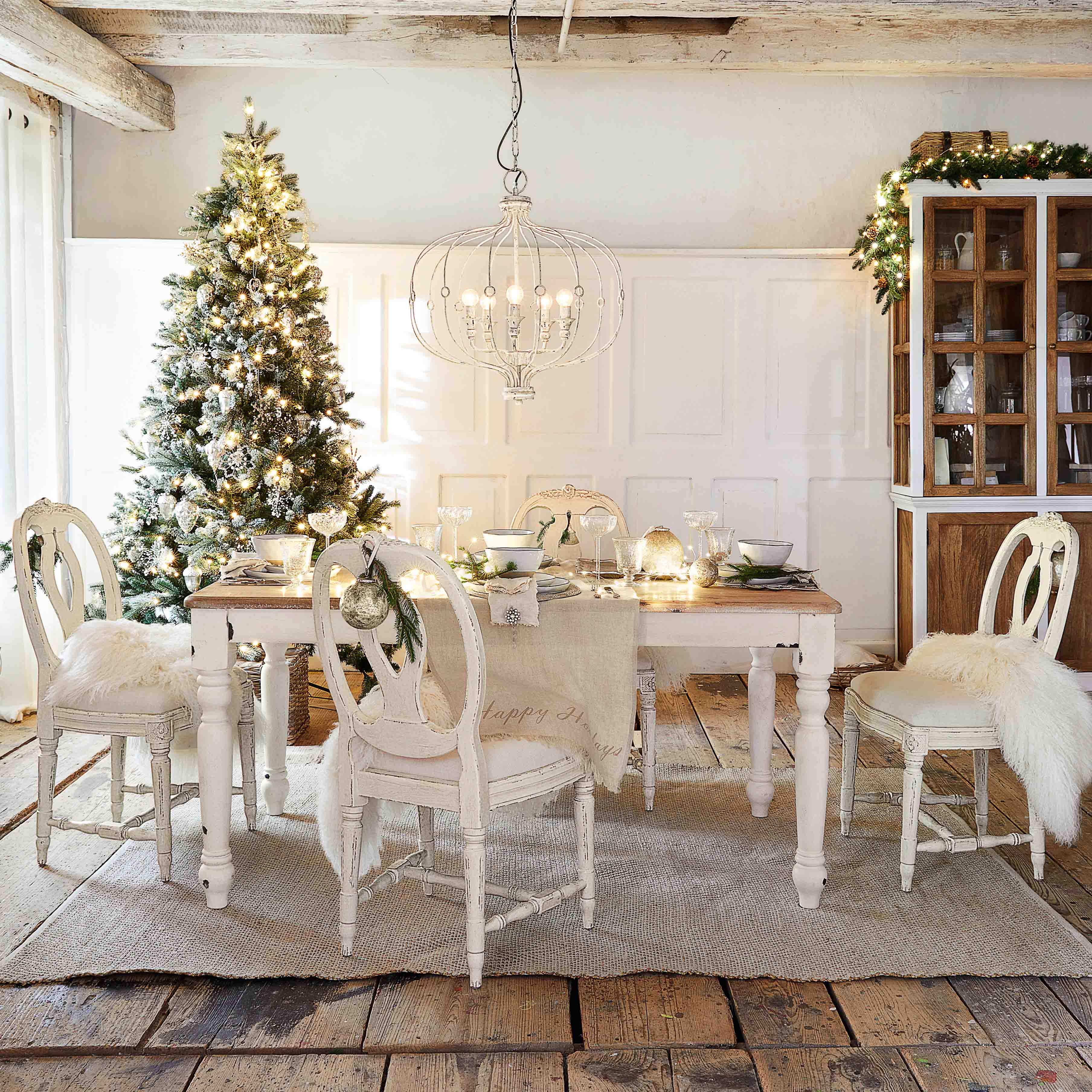 Rustikaler Essbereich mit weißem Holztisch und Stühlen, festlich dekoriert mit Weihnachtsbaum und Kronleuchter