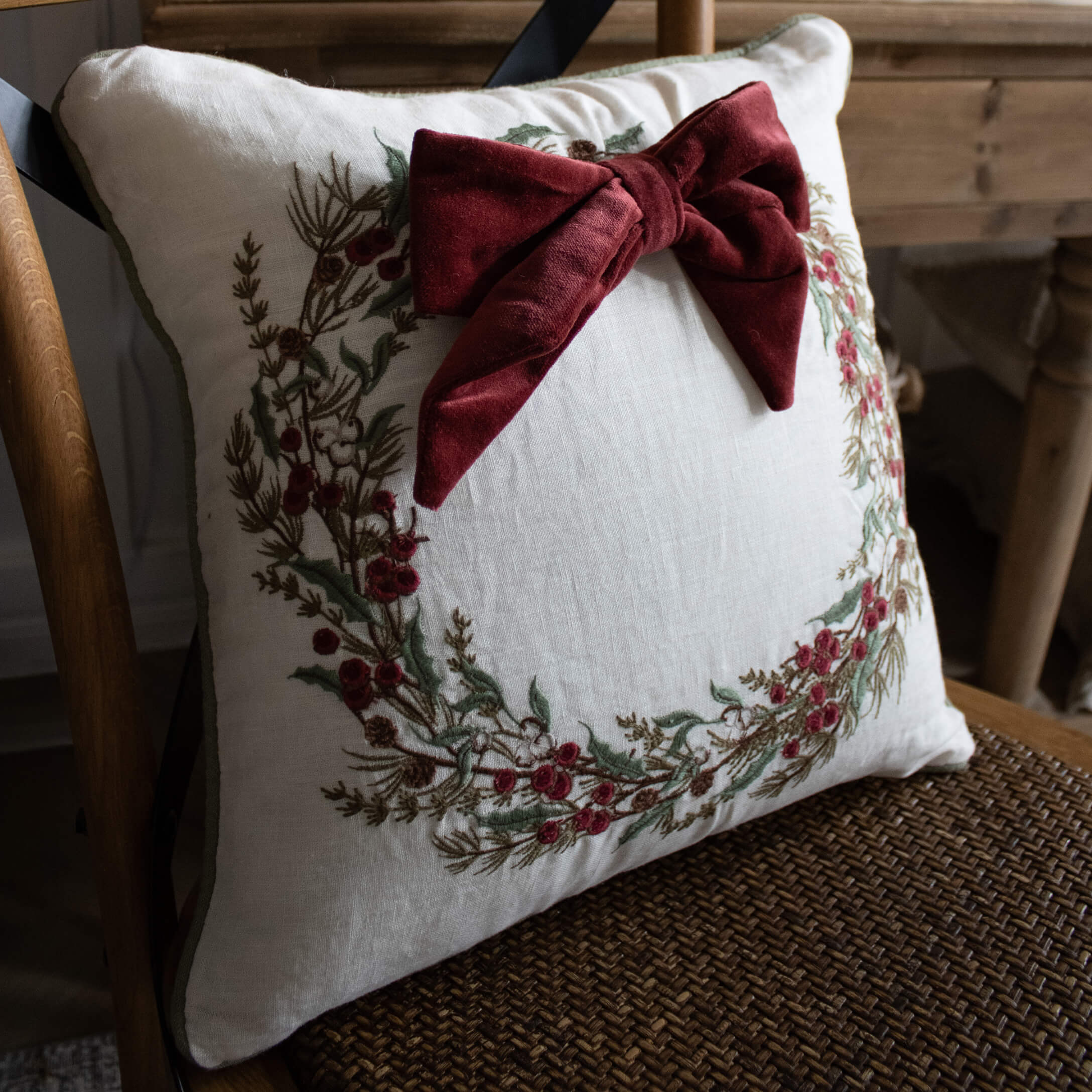 Weiße Leinenkissen mit besticktem Kranz und bordeauxroter Samtschleife, Wohnaccessoire