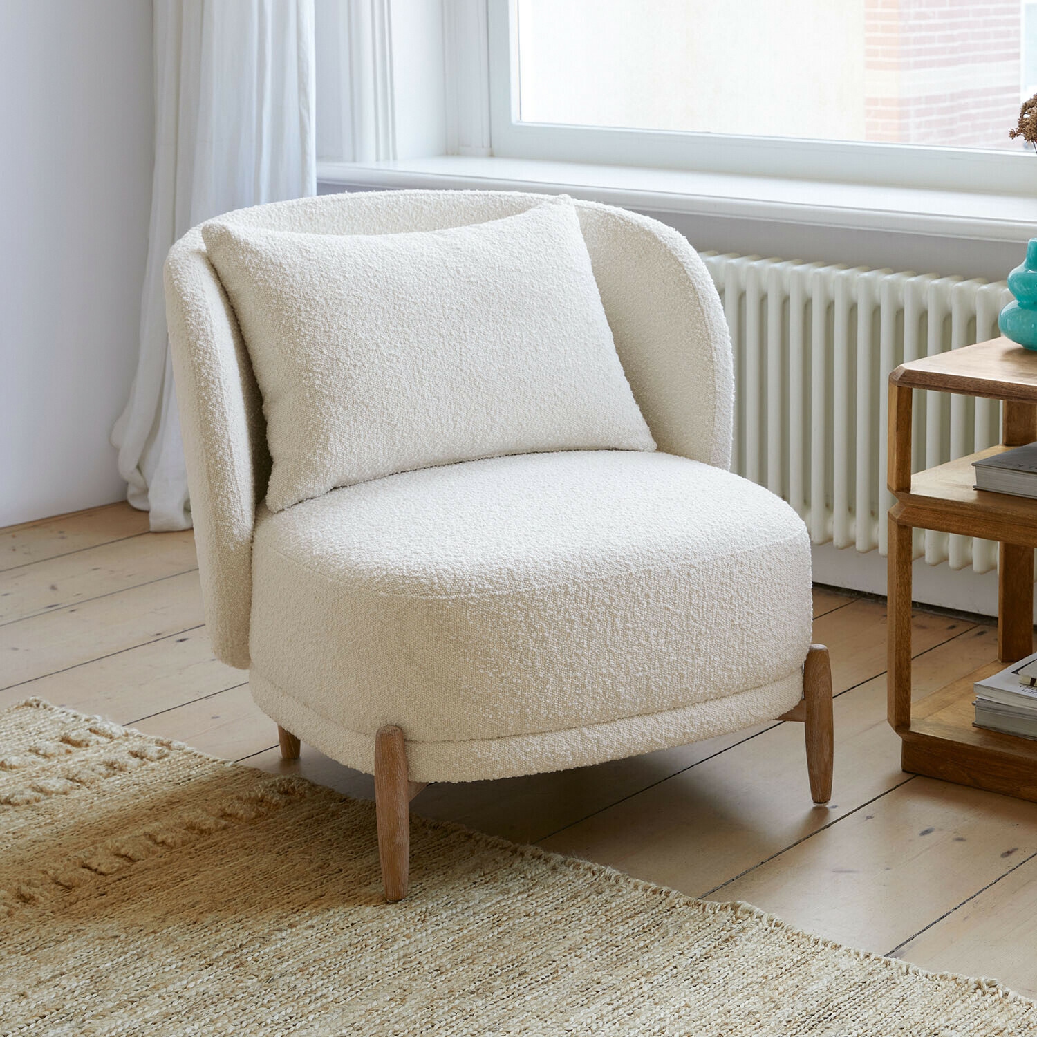 Sessel Thamira Weißer Sessel aus weichem Bouclé-Stoff mit Holzbeinen in hellem Wohnzimmer