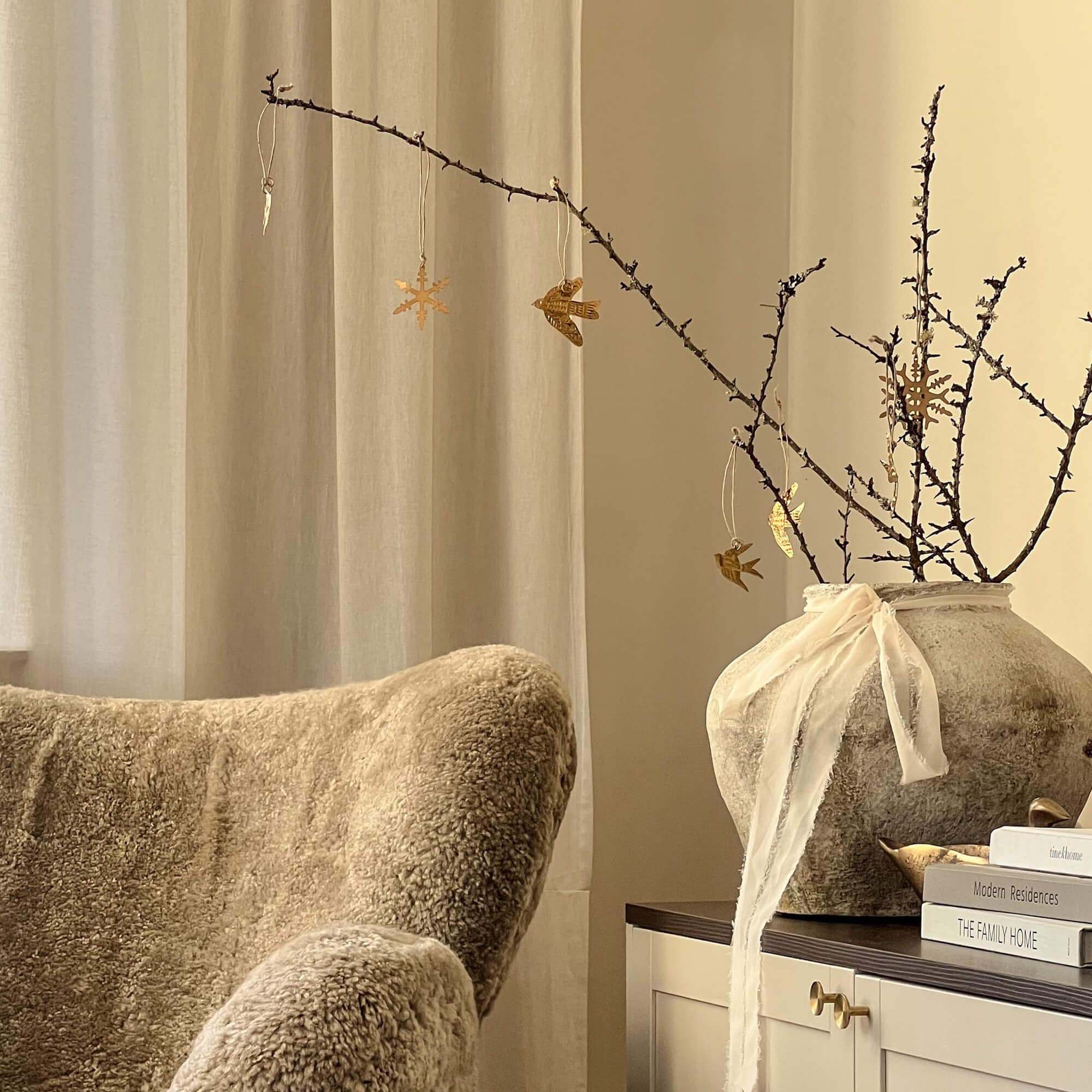 Gemütliche Winterecke mit beigem Fell-Sessel und dekorativem Vase mit Zweigen und goldenen Anhängern