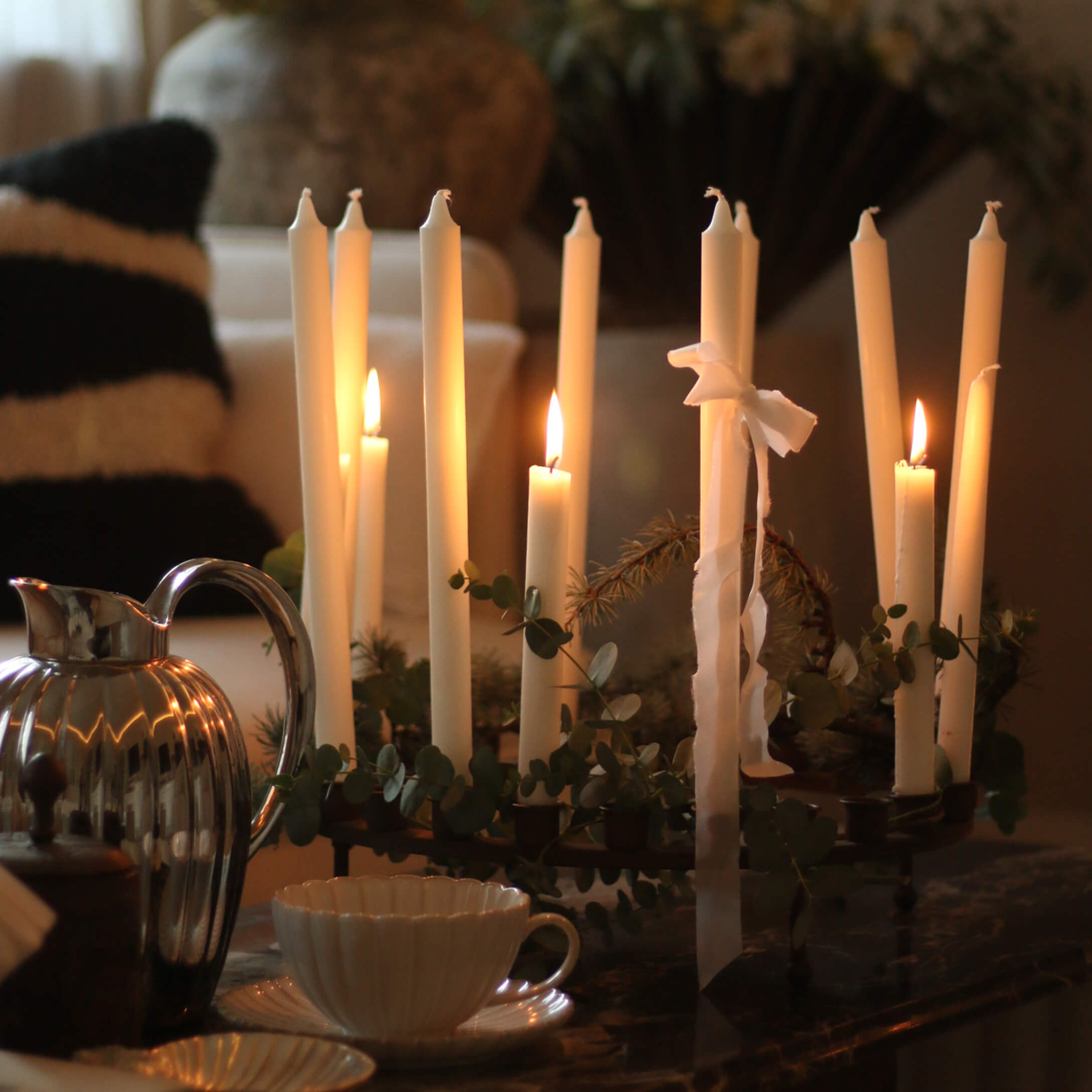 Dekorativer Kerzenhalter mit weißen Kerzen und grünen Blättern auf Tisch in gemütlichem Raum