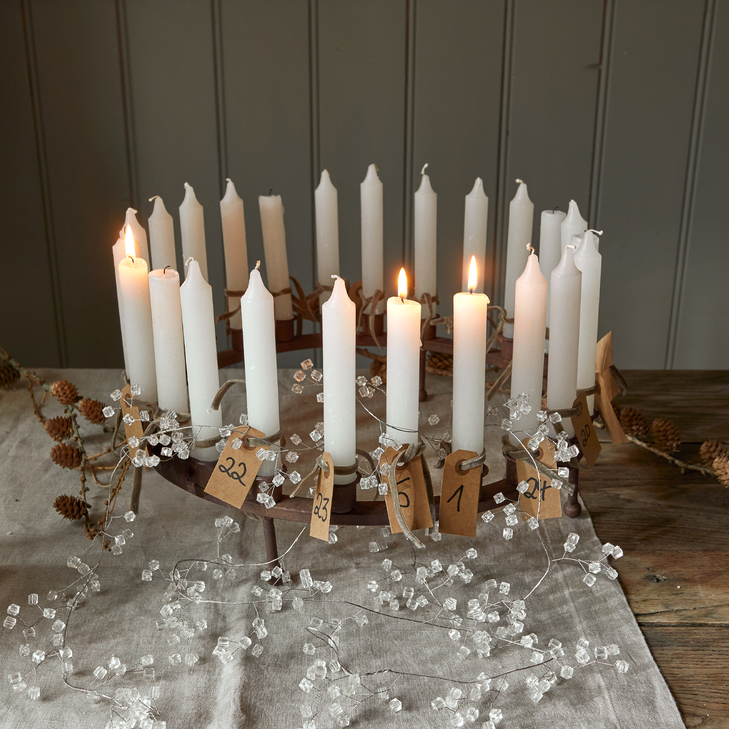 Metall-Adventskranz mit 24 weißen Kerzen und nummerierten Papieranhängern auf Leinentuch mit Dekoration