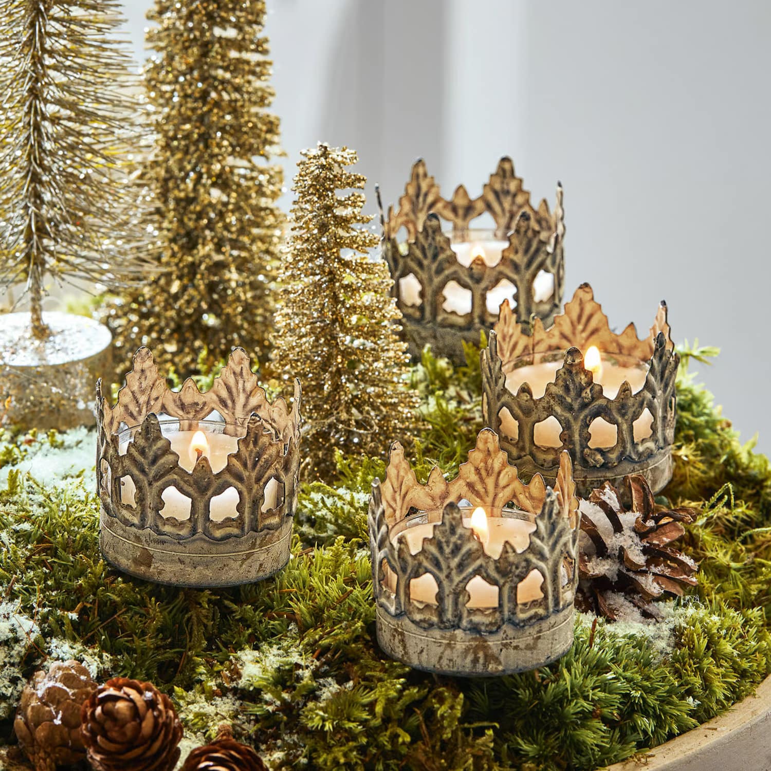 Metall-Kerzenhalter in Kronenform auf grünem Moos mit Weihnachtsdeko und goldenen Bäumchen