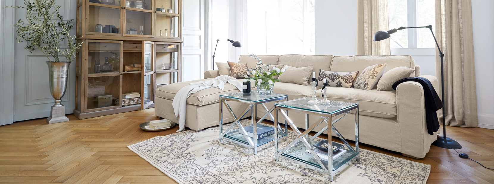 Klassisch elegantes Wohnzimmer mit beigem Sofa, gläsernen Tischen und Holzvitrine auf hellem Parkett