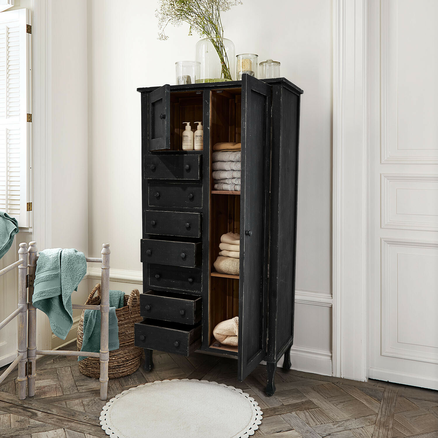 Schwarzer Holzschrank mit Schubladen und Regalen, gefüllt mit Handtüchern und Pflegeprodukten