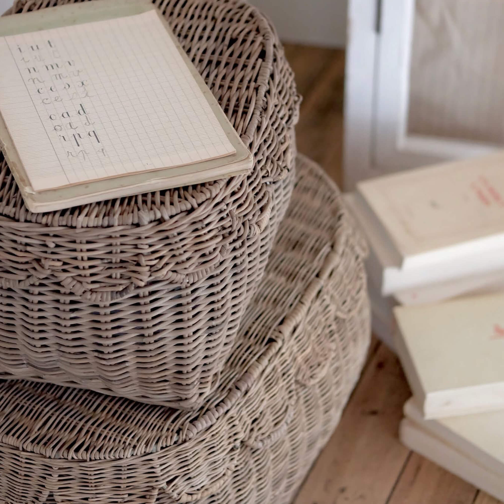 Beige geflochtene Rattankörbe gestapelt auf Holzboden mit Notizbuch obenauf