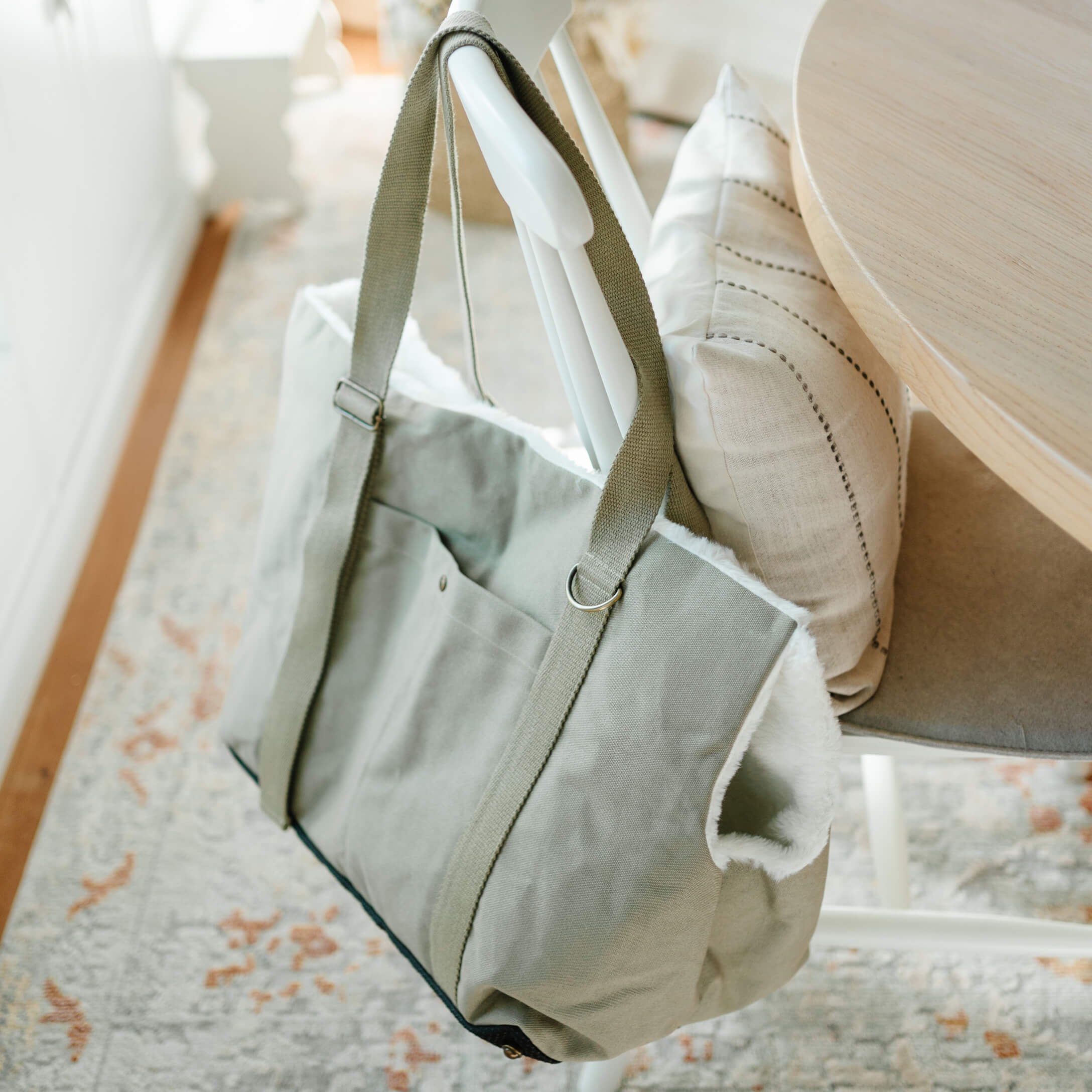 Graue Stofftasche mit weißem Fellfutter hängt an weißem Stuhl in hellem Raum