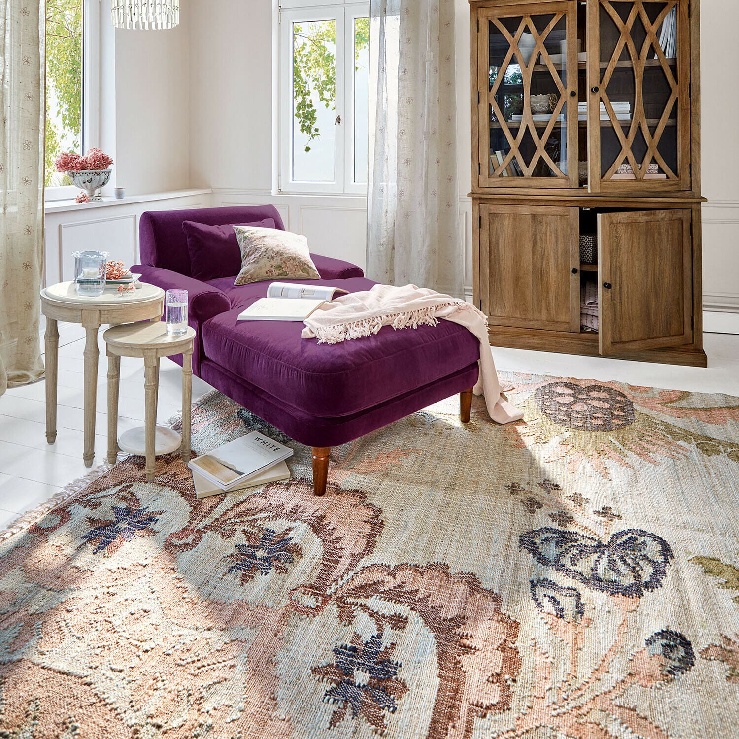 Teppich Amélorie Violette Samt-Chaiselongue in hellem Wohnzimmer mit Holzvitrine und dekorativem Teppich
