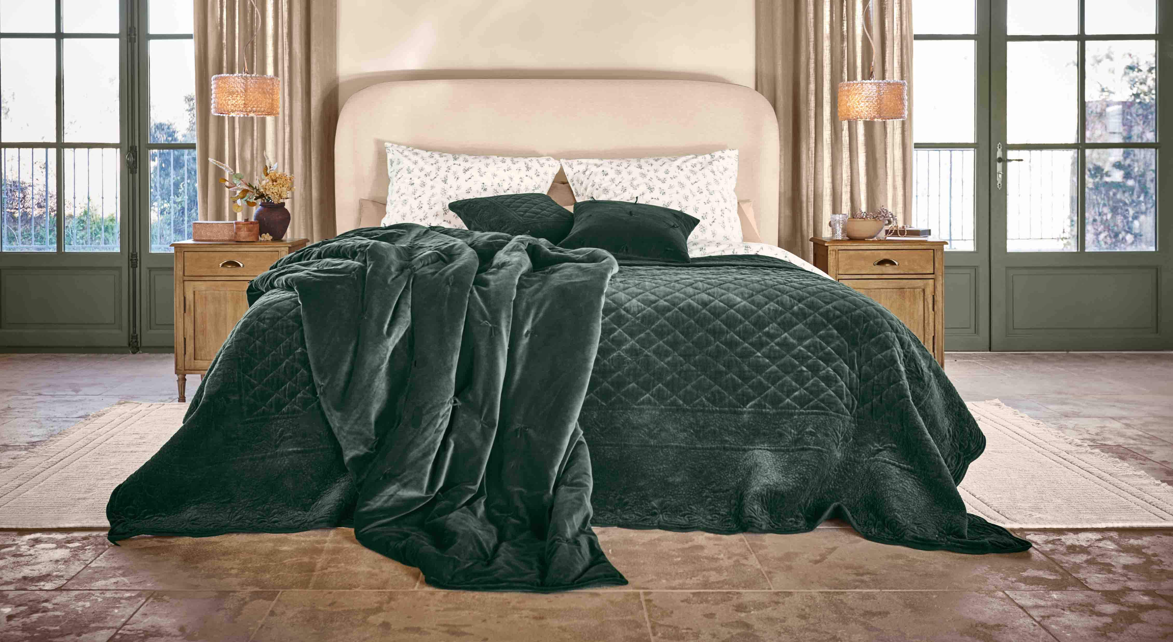 Gemütliche dunkelgrüne Steppdecke und Kissen aus weichem Material auf Bett in hellem Schlafzimmer