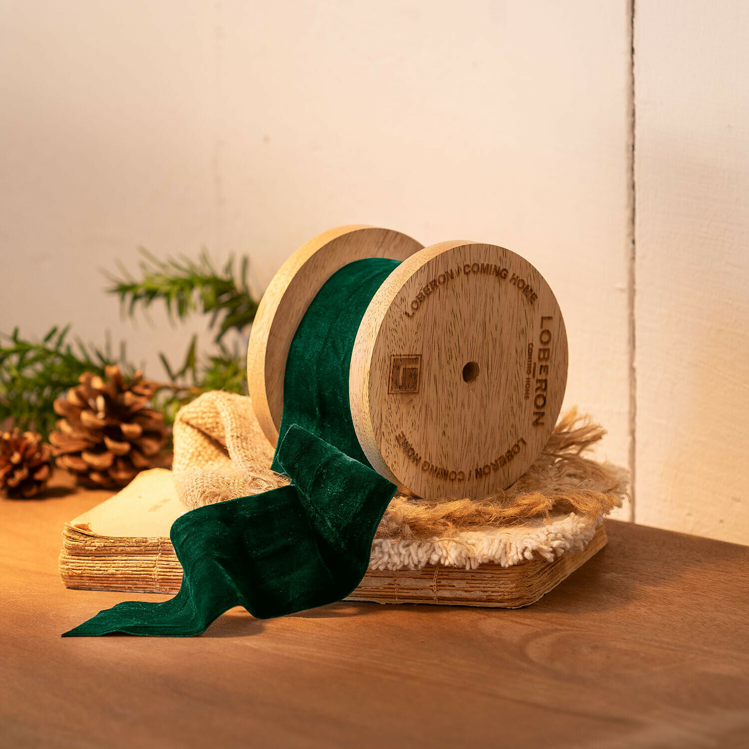 Samtband Phaedra Holzspule mit grünem Samtband auf rustikalem Hintergrund mit Tannenzapfen und altem Buch