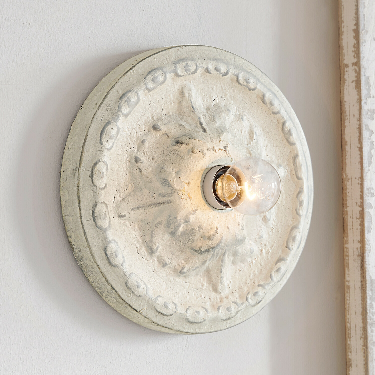Runde Wandlampe aus hellem Beton mit dekorativem Muster und leuchtender LED-Glühbirne
