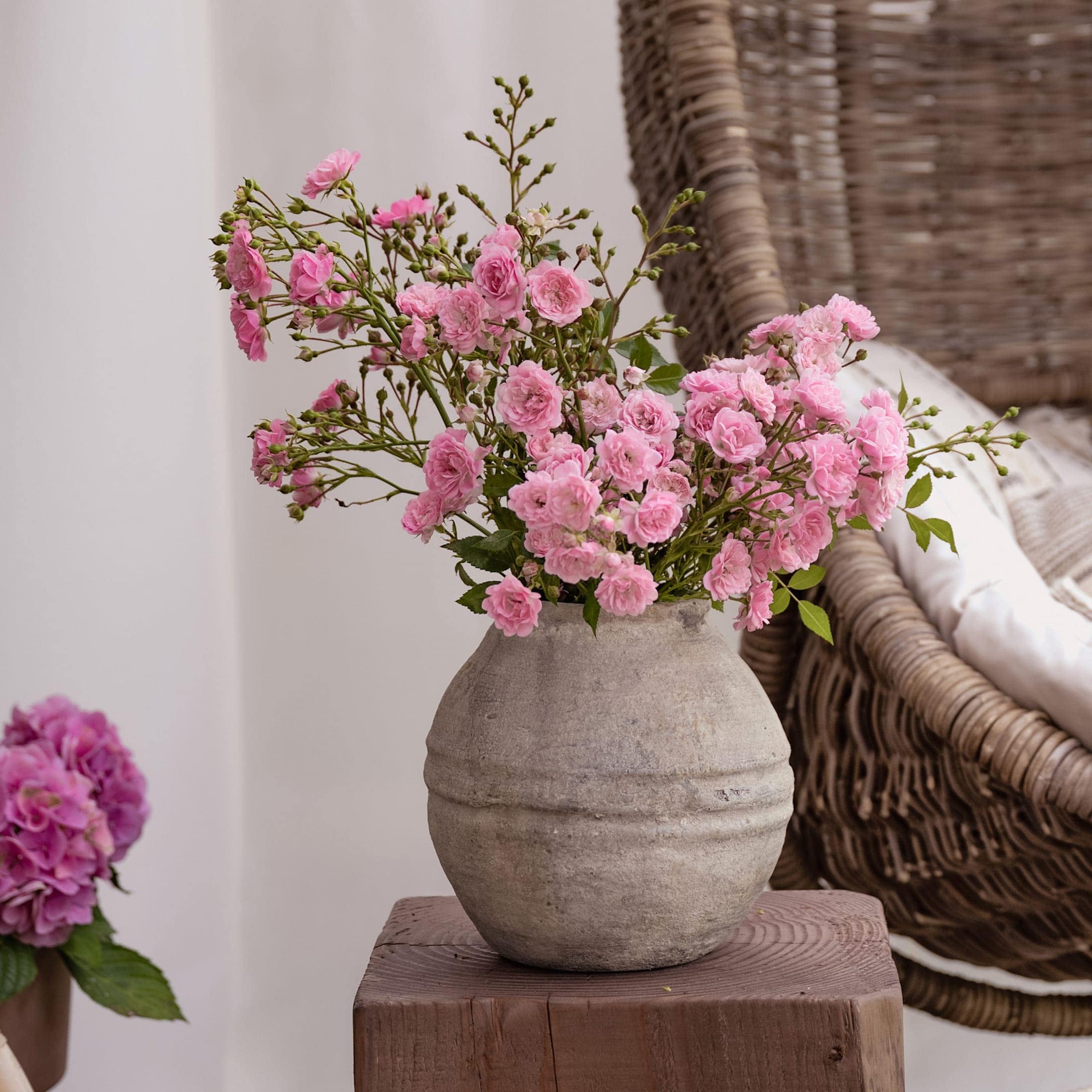 Grauer Keramikvase mit rosa Blumen auf Holzblock, stilvolle Wohnraumdekoration
