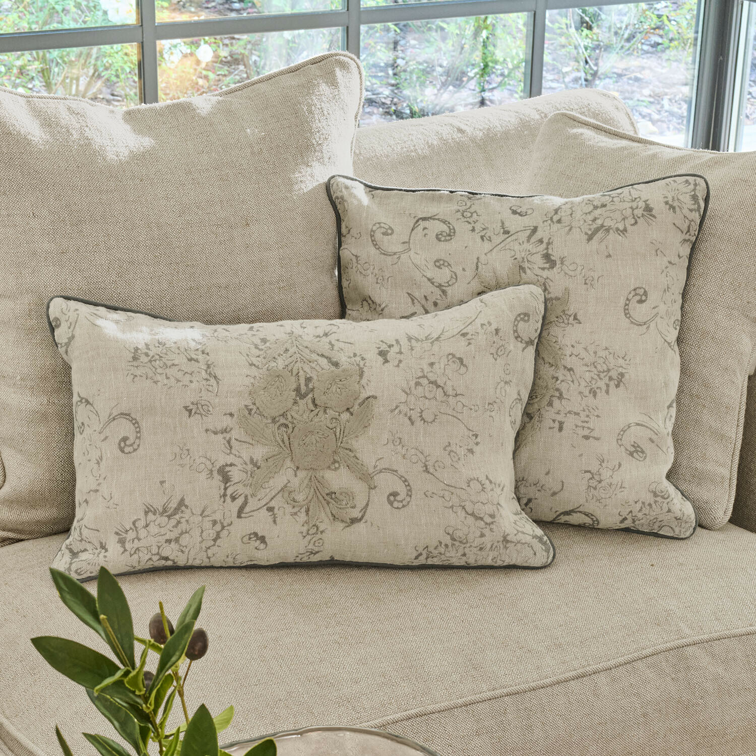 Beige Leinen-Dekokissen mit floralem Muster auf hellem Sofa im Wohnzimmer