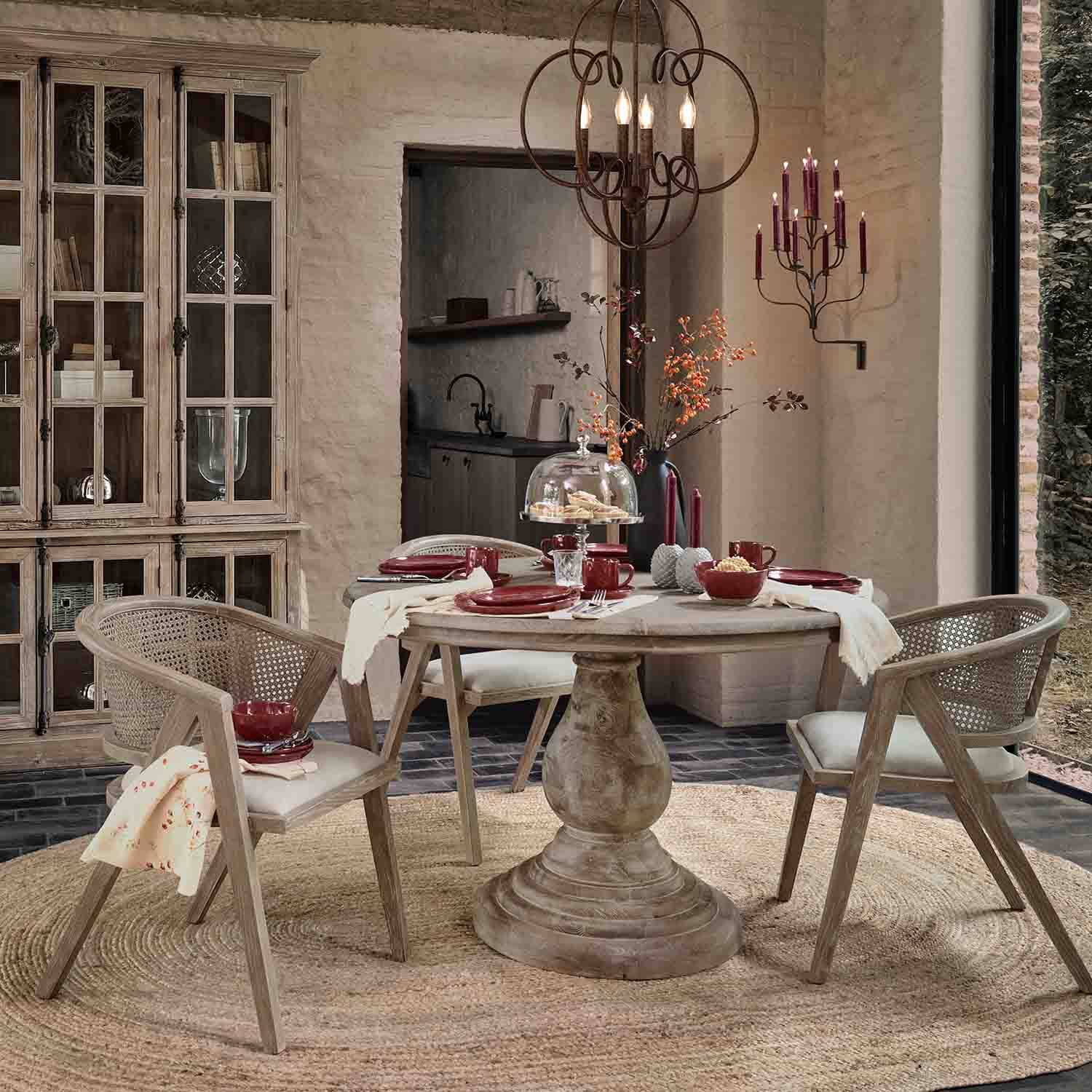 Esszimmer mit rundem Holztisch und Rattanstühlen in Naturtönen, bordeauxfarbene Dekorationen