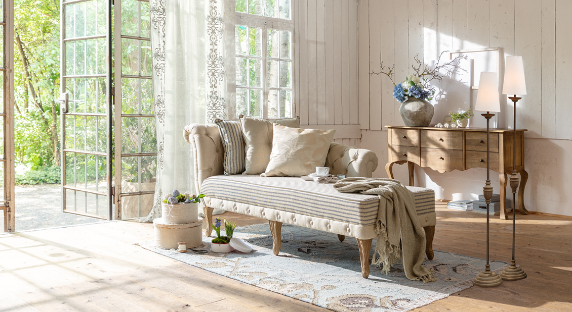 Beige gepolsterte Chaiselongue mit Holzbeinen und Kissen in hellem Wohnzimmer mit natürlichem Licht