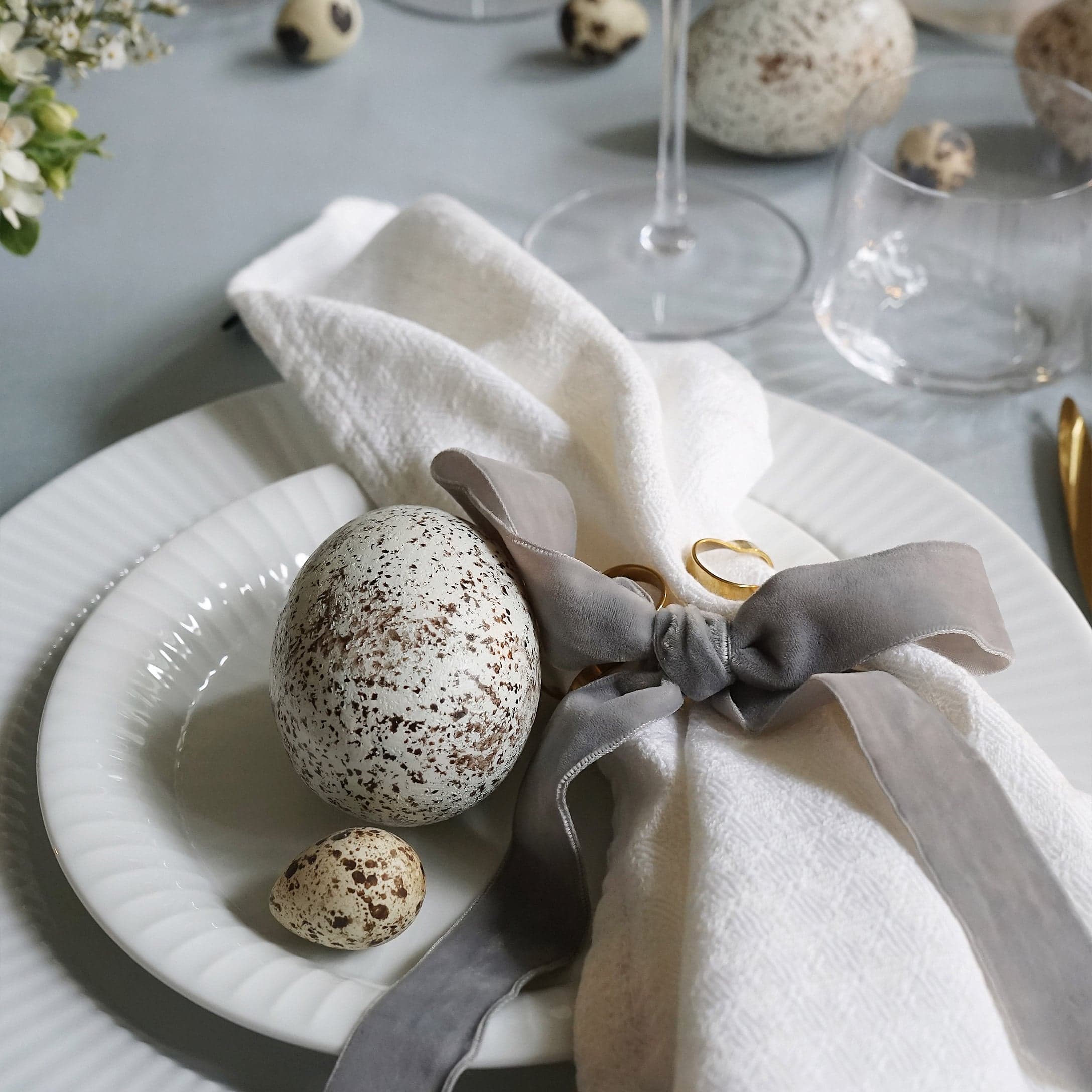 Weiße Teller mit dekorativen gesprenkelten Eiern und Leinenserviette mit grauer Schleife auf Tisch