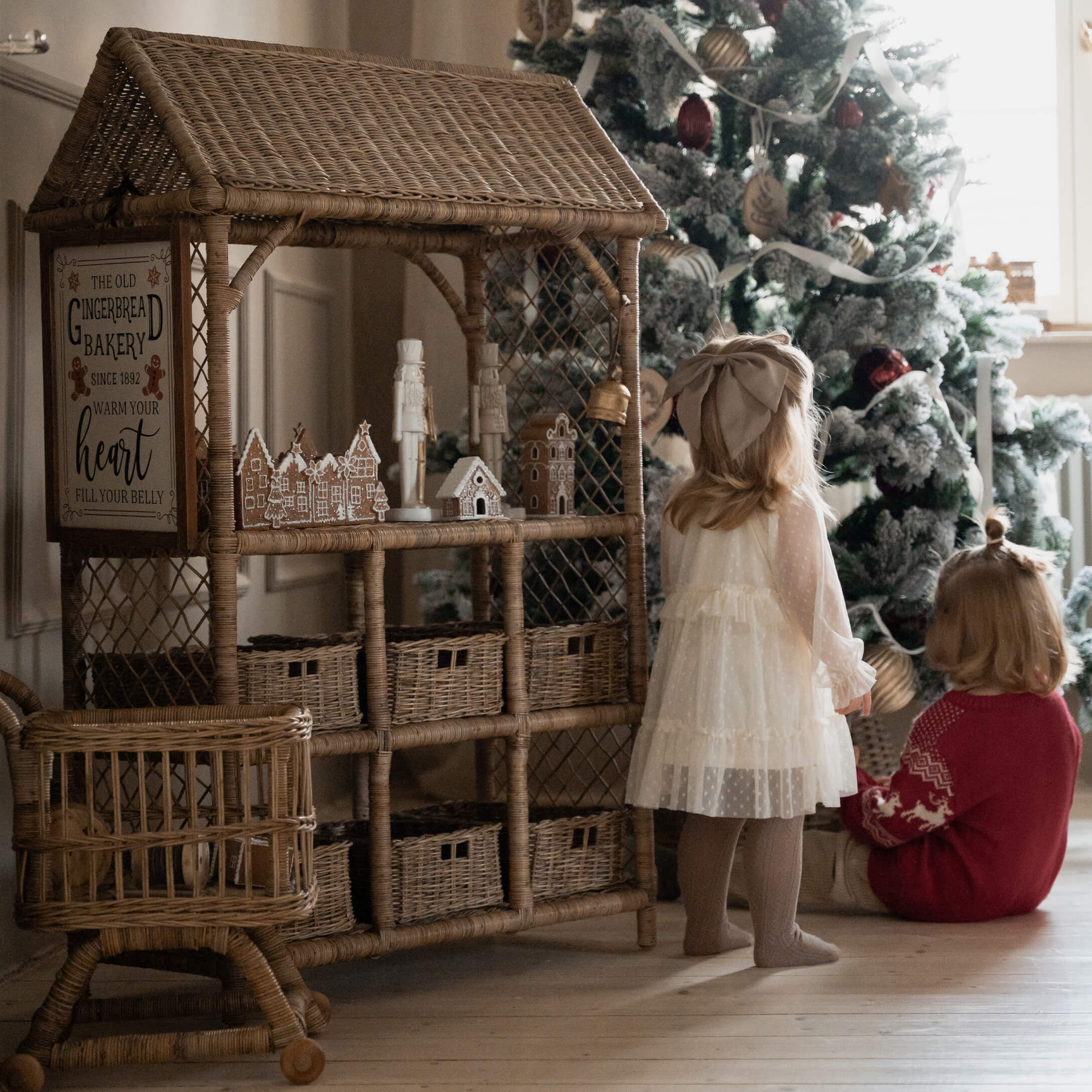 Wickelhaus aus Rattan mit Lebkuchendekorationen neben Kindern vor geschmücktem Weihnachtsbaum
