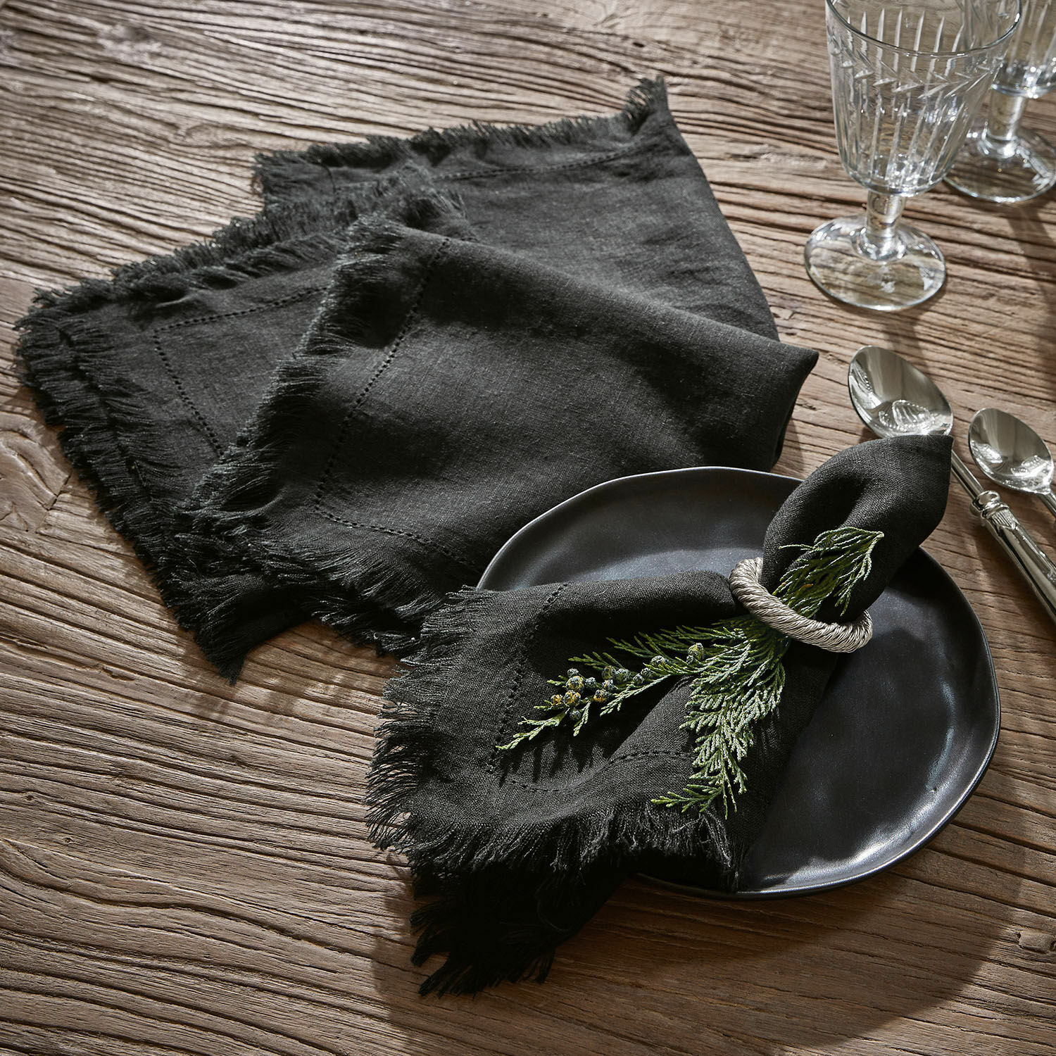 Serviette 4er Set Pibrac Schwarze Leinenservietten mit Fransen auf Holztisch mit grüner Zweig-Dekoration