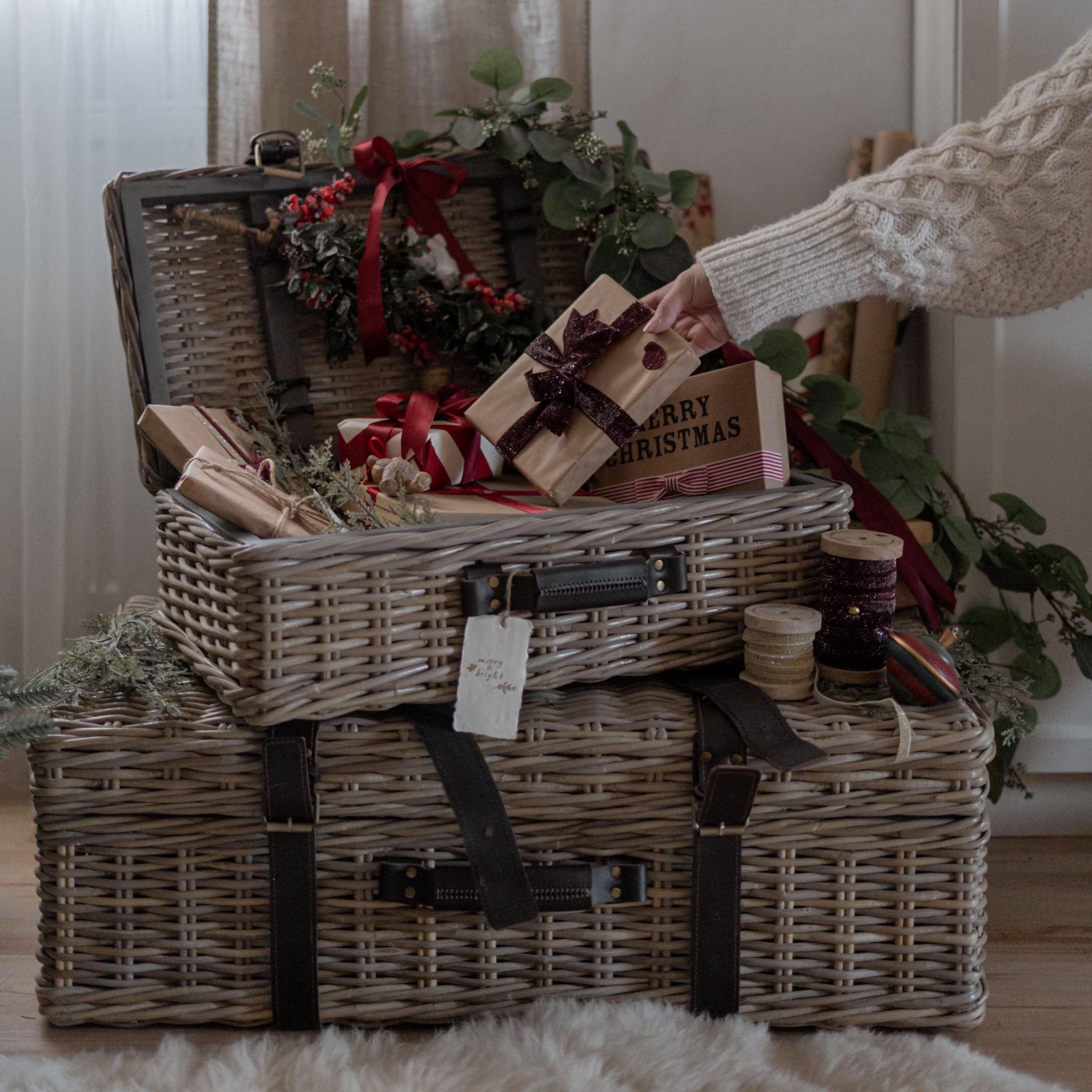 Zwei graue Rattankörbe mit dunklen Lederriemen, geschmückt mit Weihnachtsgeschenken und Dekorationen