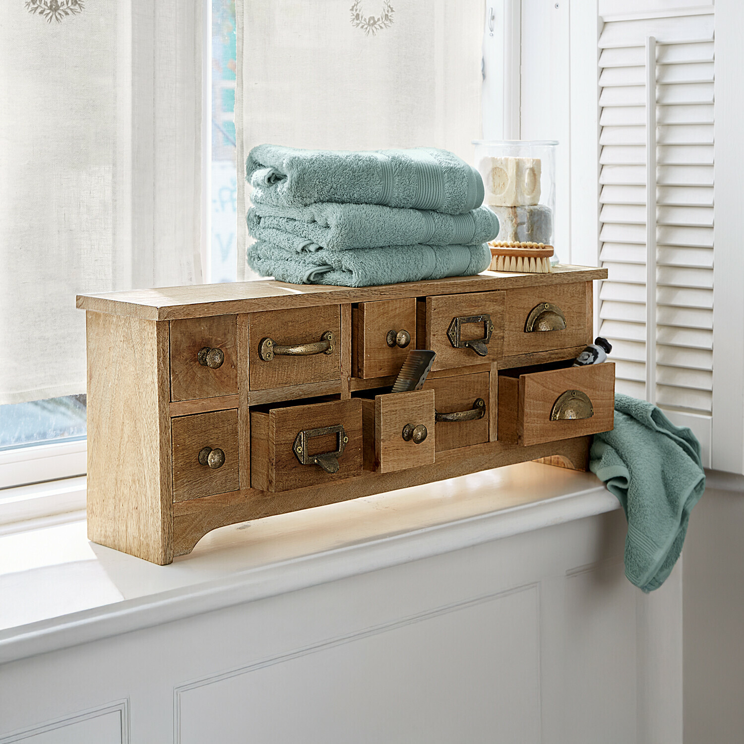 Holzkommode mit vielen Schubladen und weichen grünen Handtüchern auf dem Fensterbrett