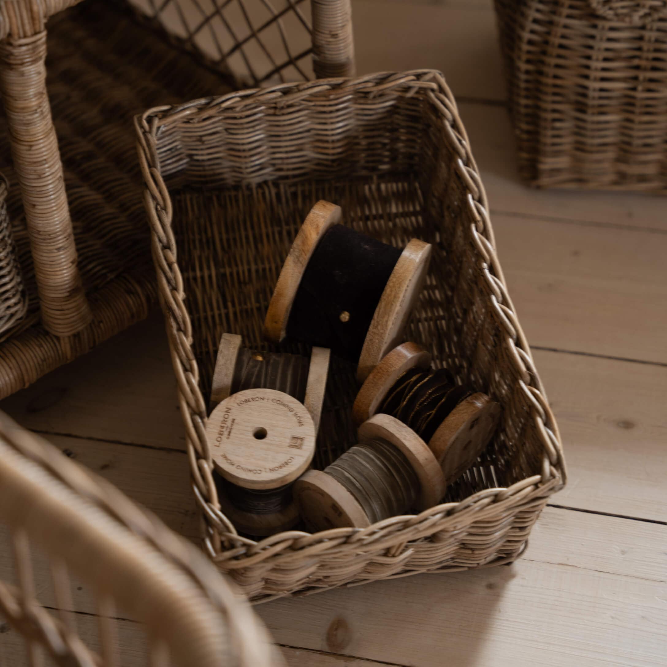 Wikingerkorb mit Holzspulen und schwarzem sowie grauem Garn auf hellem Holzboden