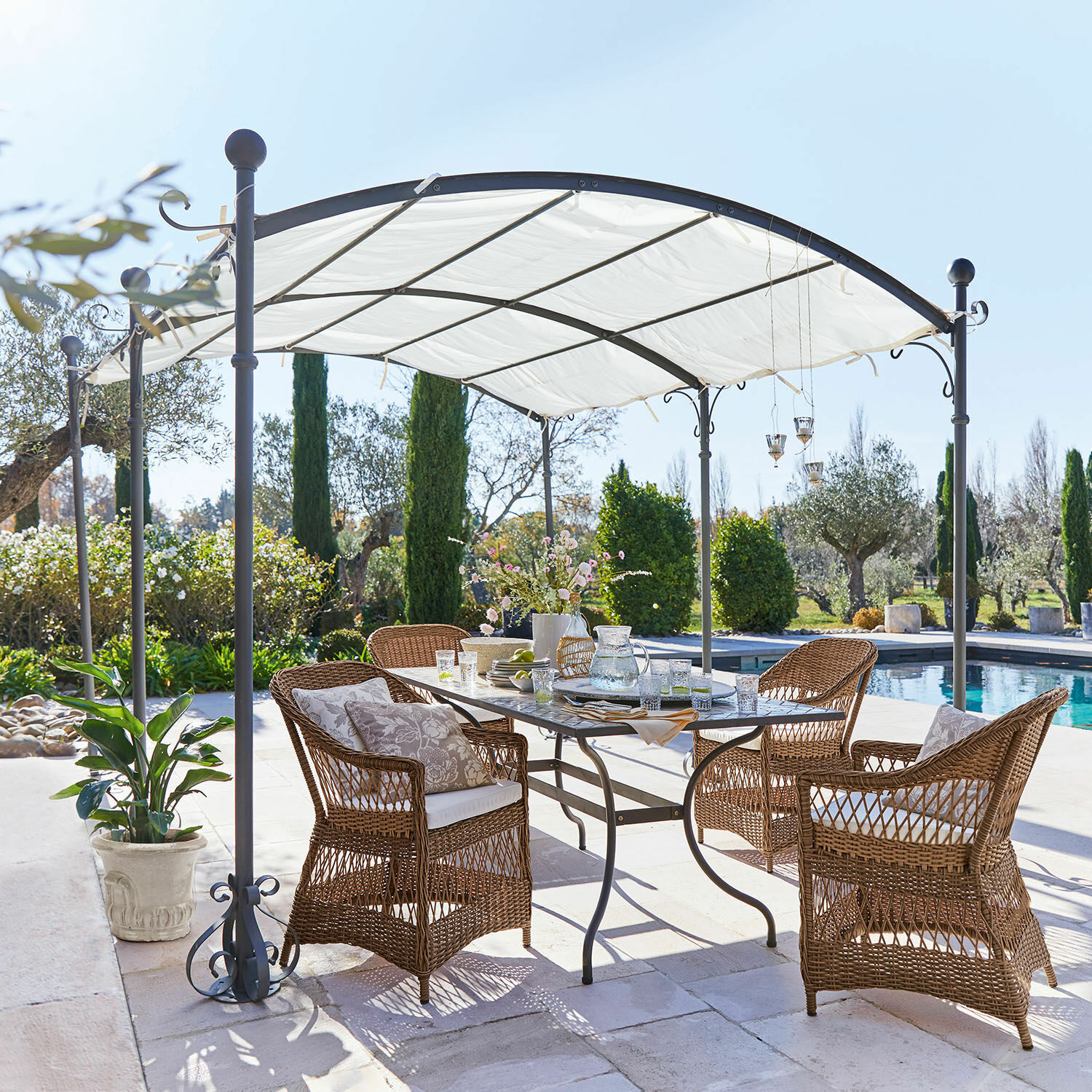 Pergola Yarl Gartenmöbel-Set aus braunem Rattan unter weißem Metallpavillon neben Pool