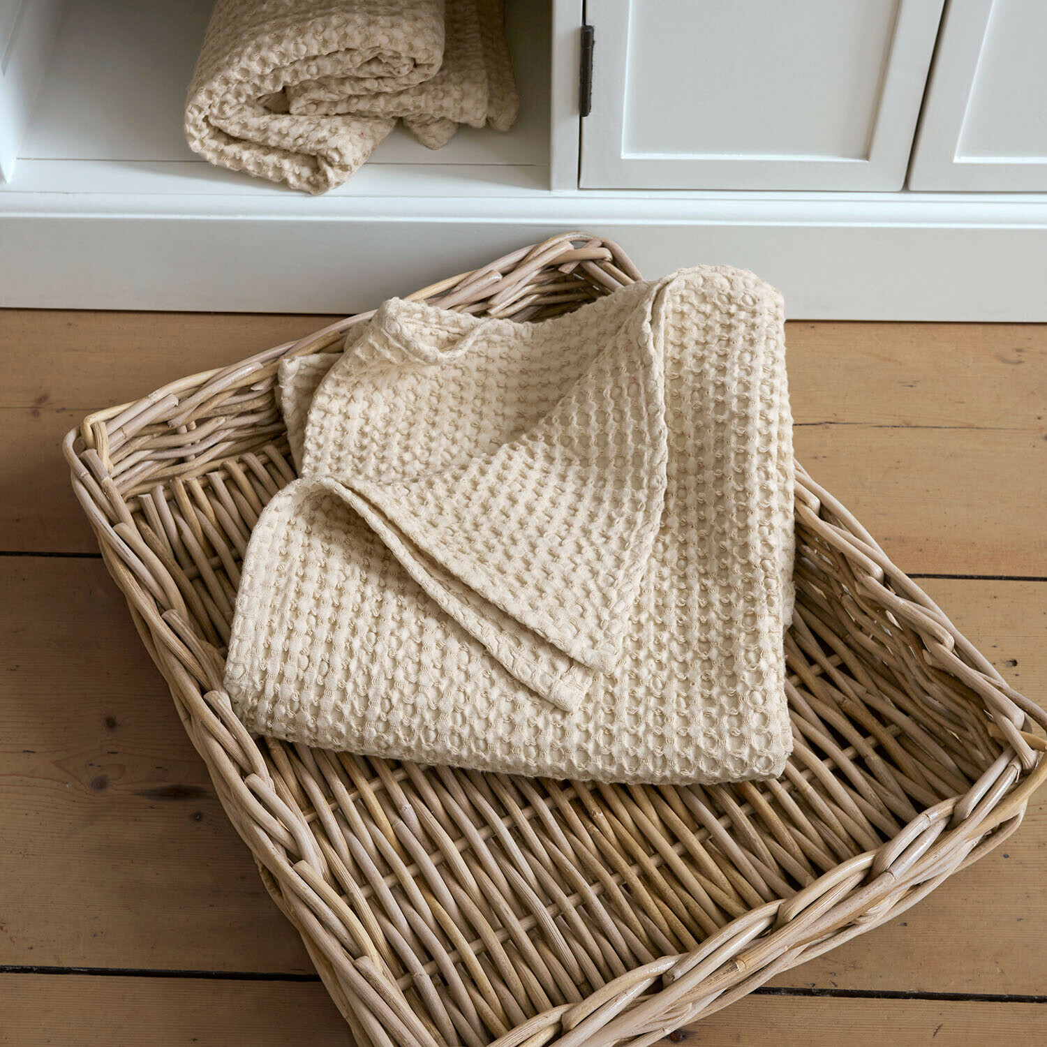 Handtuch Maralei Beige Baumwoll-Waffeldecke in einem Korb aus Weide auf hellem Holzboden
