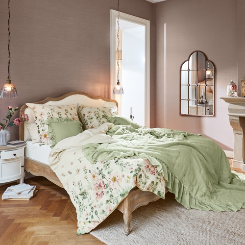 Schlafzimmer mit Holzbett, grüner und geblümter Bettwäsche, hängender Lampe und dekorativem Wandspiegel