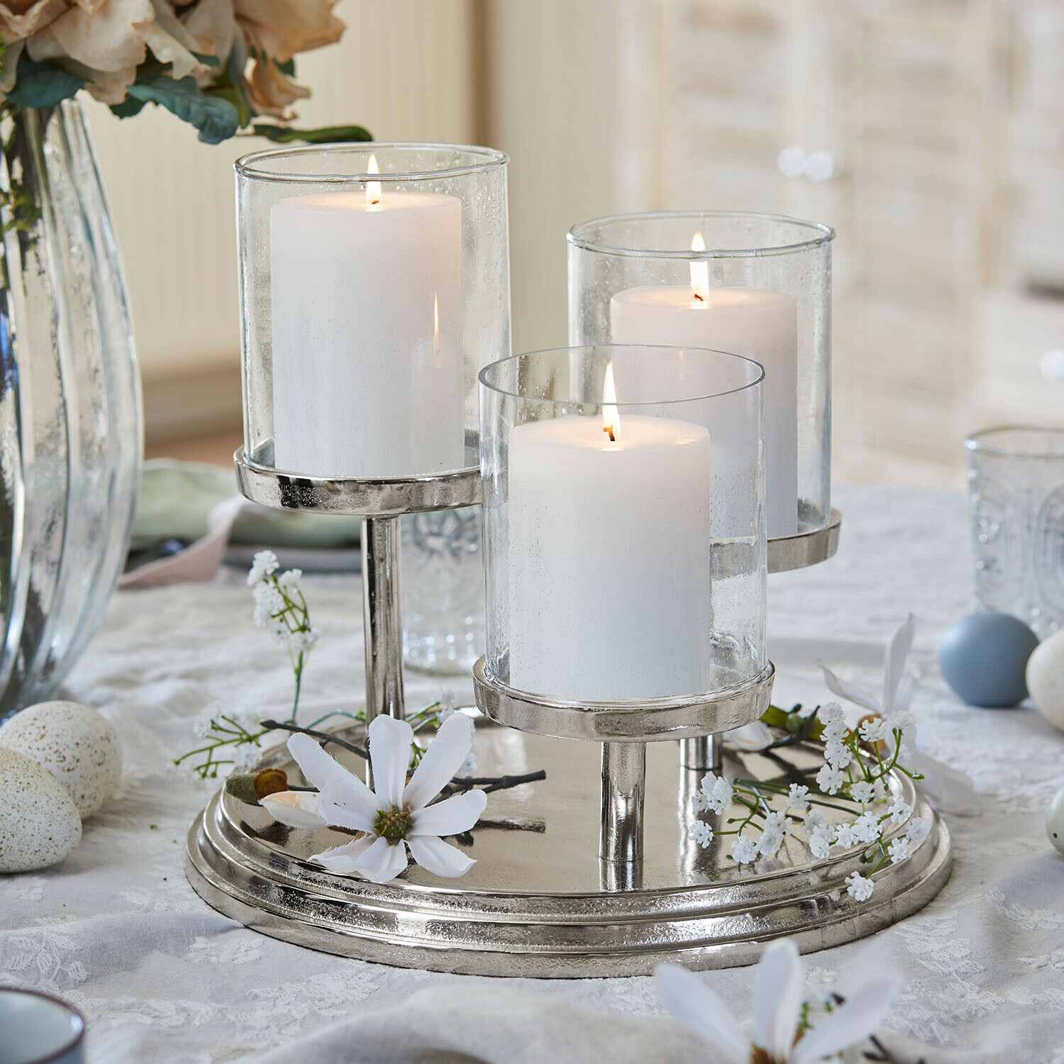 Dreifacher Metall-Kerzenhalter mit weißen Kerzen und Glasaufsätzen als Tischdekoration