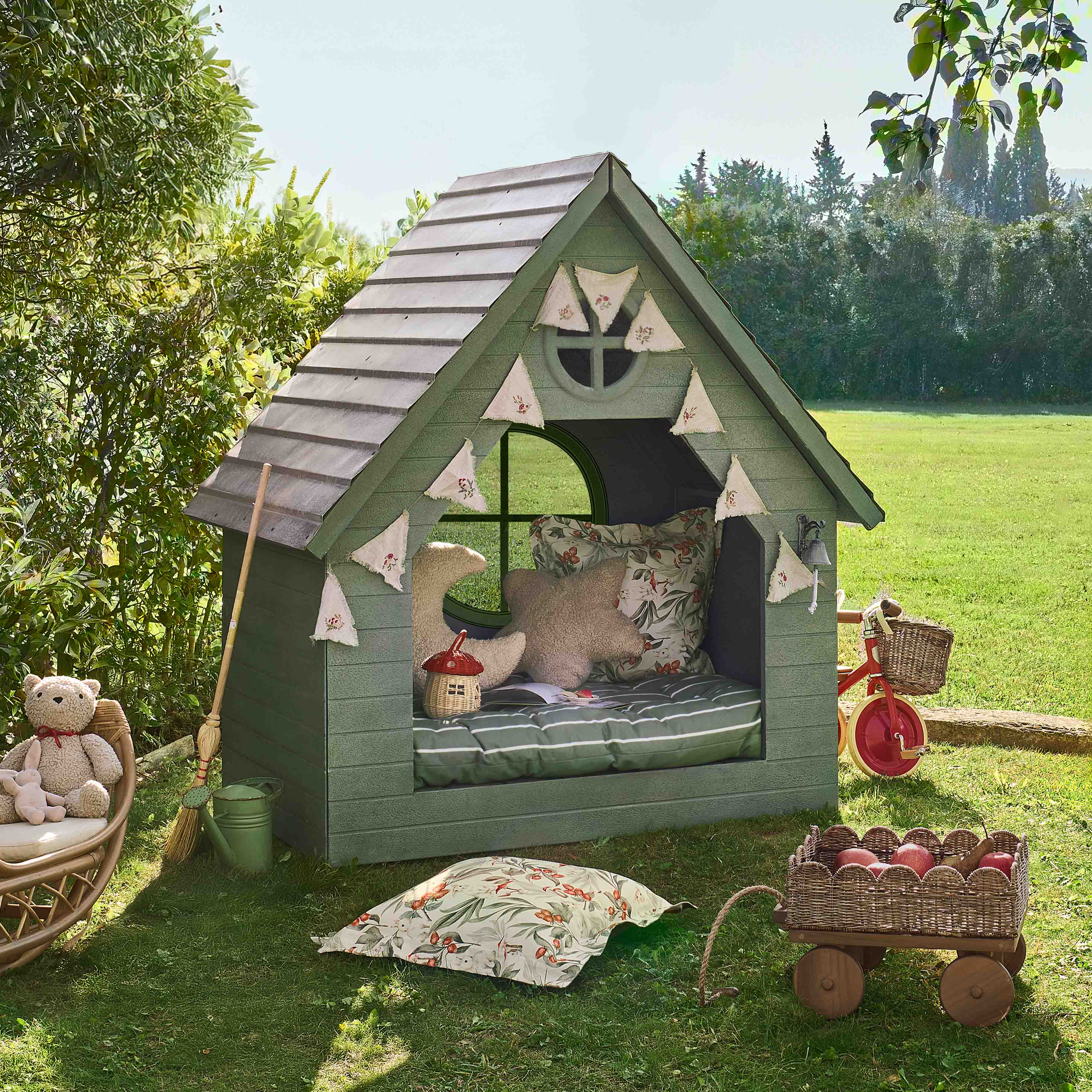Grünes Holz-Kinderhaus mit Kissen und Dekorationen auf Gras im Garten