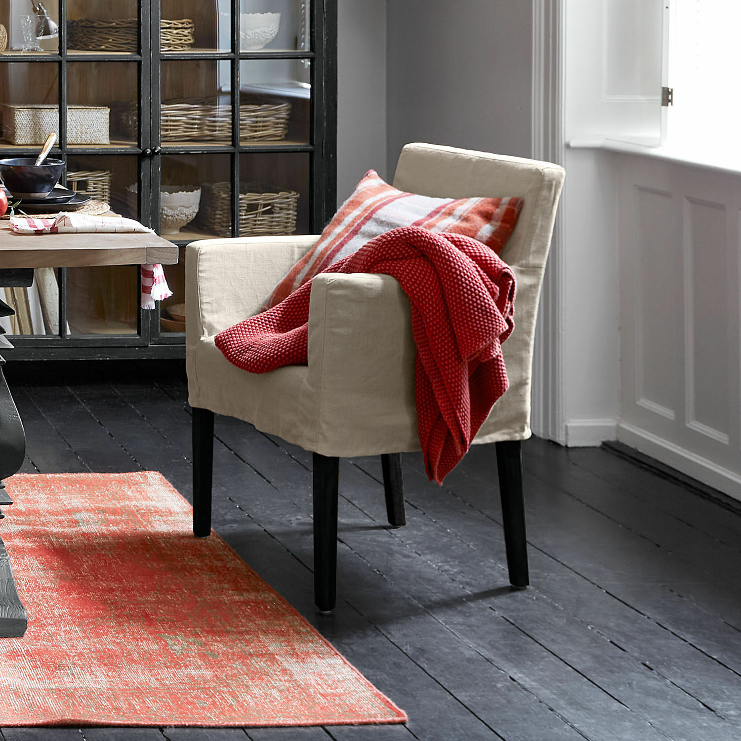 Beiger Stoffsessel mit schwarzen Beinen, roter Decke und kariertem Kissen, roter Teppich