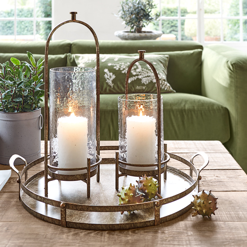 Metalltablett mit zwei Glaslaternen und weißen Kerzen auf hellem Holztisch im Wohnzimmer