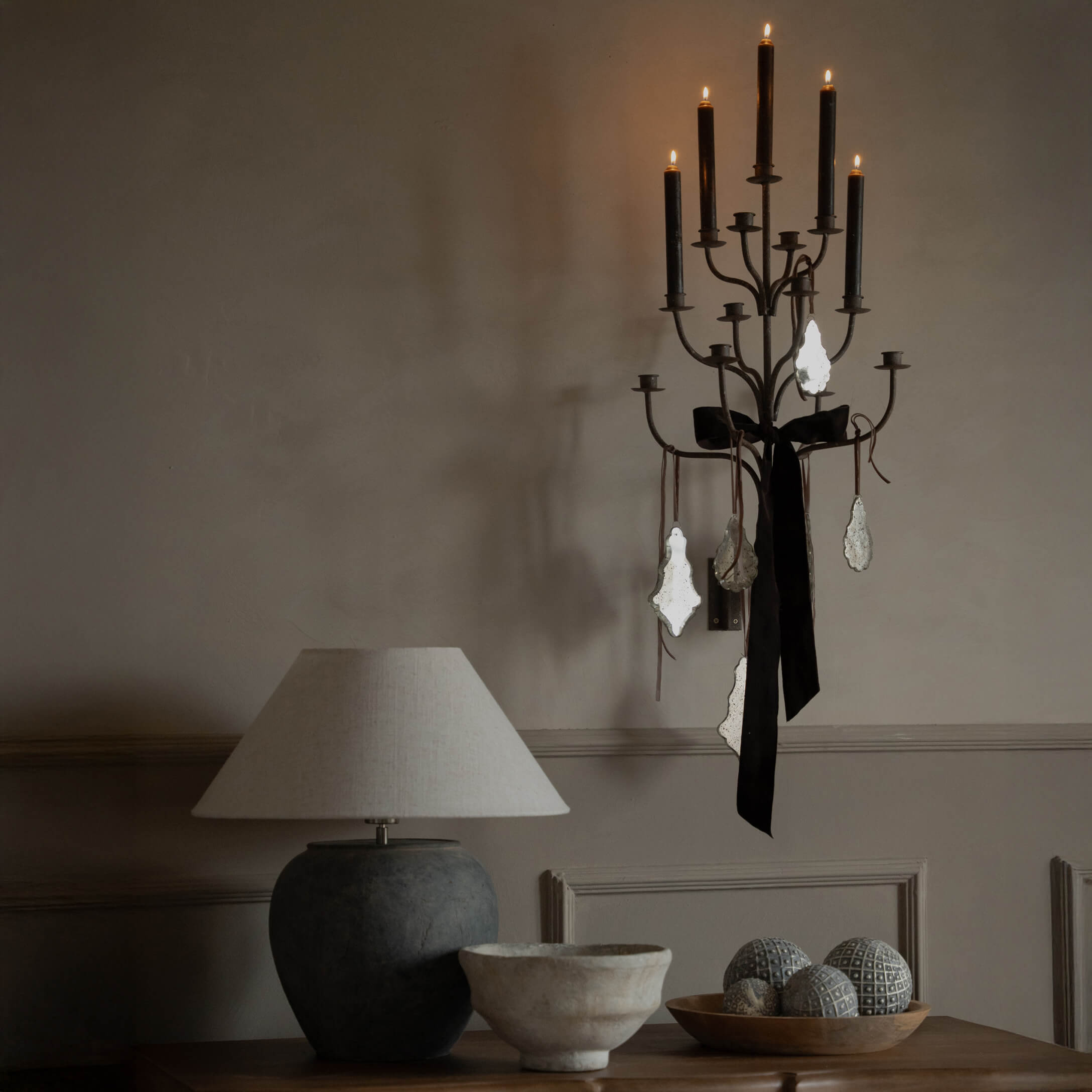 Schwarzer Metall-Wandkerzenhalter mit schwarzer Schleife und Anhängern, beige Tischlampe auf Holztisch