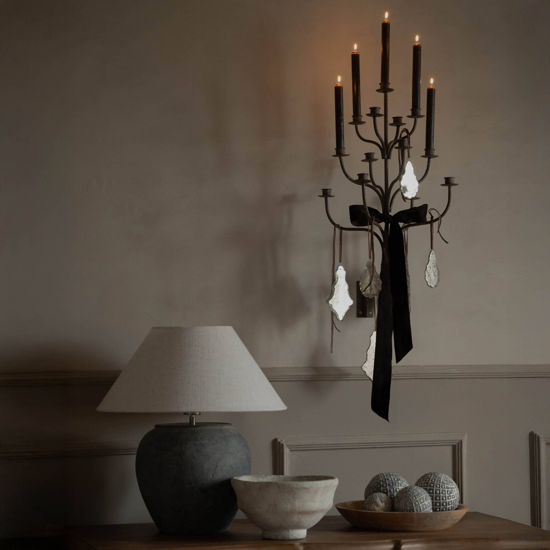 Schwarzer Metall-Wandkerzenhalter mit schwarzer Schleife und Anhängern, beige Tischlampe auf Holztisch