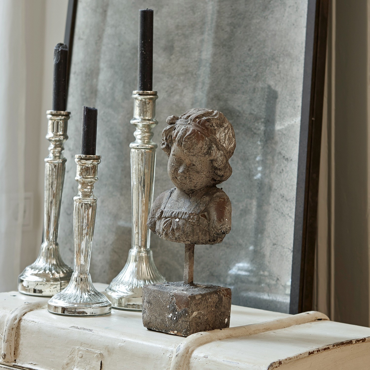 Dekorative graue Steinstatue auf weißem Möbelstück mit silbernen Kerzenhaltern im Hintergrund
