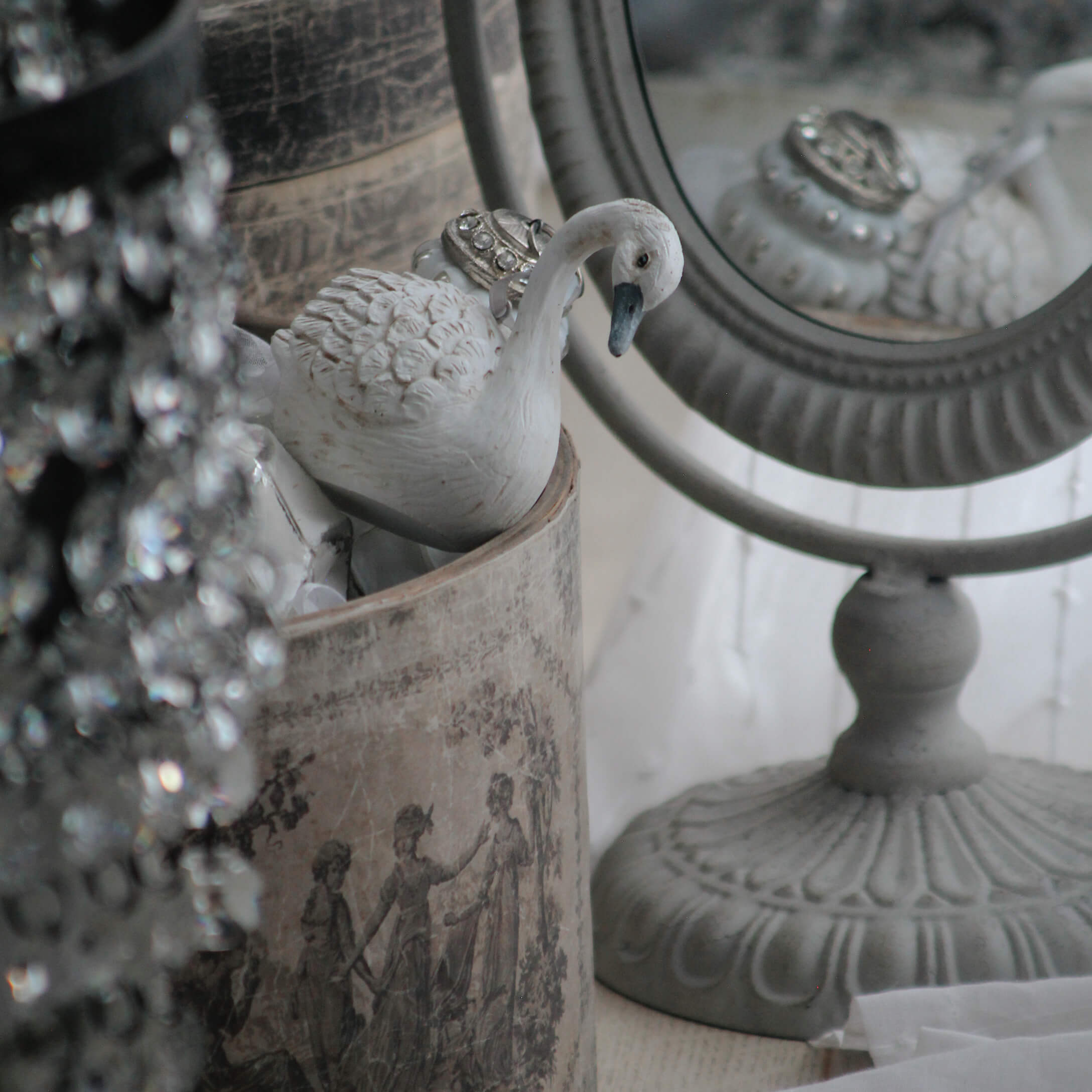 Weiße Keramikschwan-Figur neben dekorativem Spiegel und Vintage-Behälter mit klassischem Muster