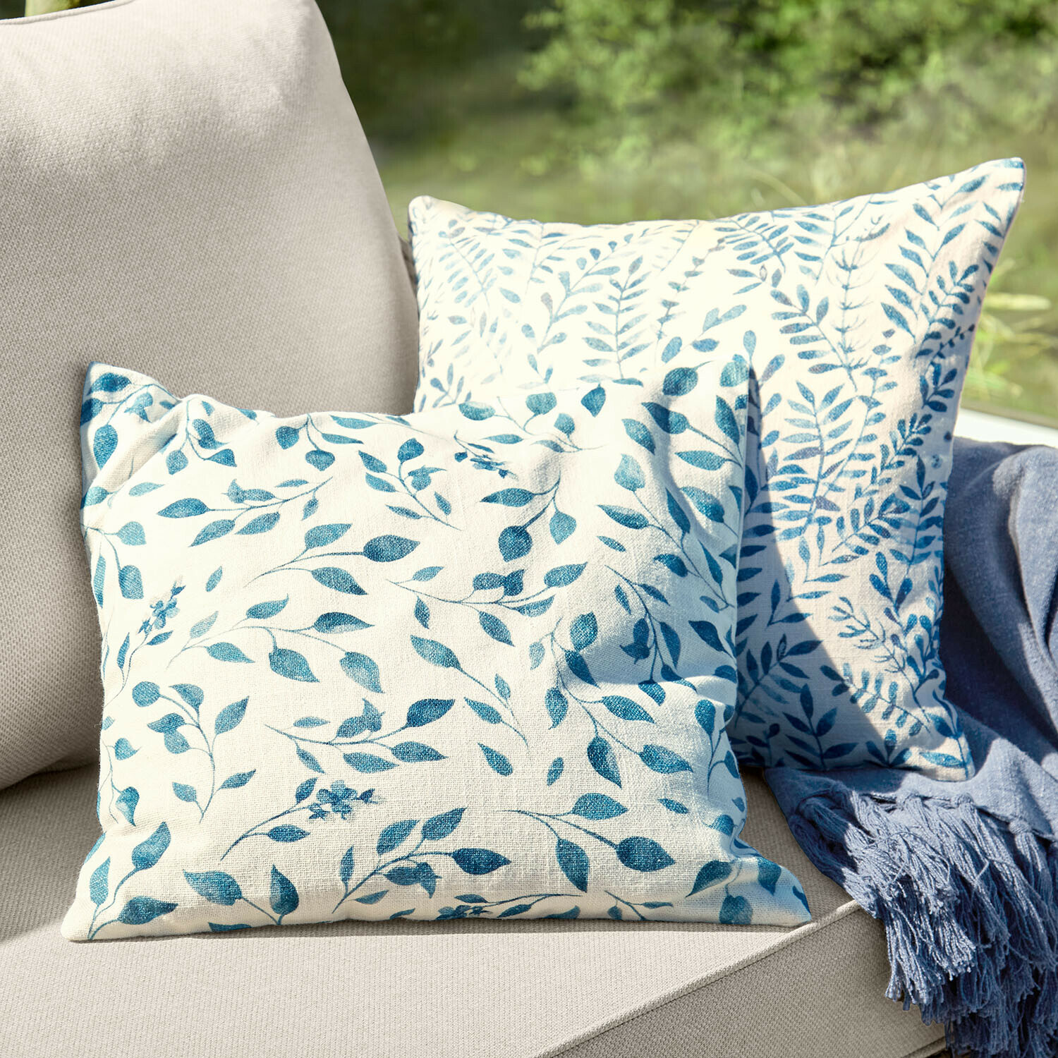 Kissenhülle 2er Set Ocevara Zwei dekorative Baumwollkissen in Creme mit blauem Blattmuster auf beigem Sofa