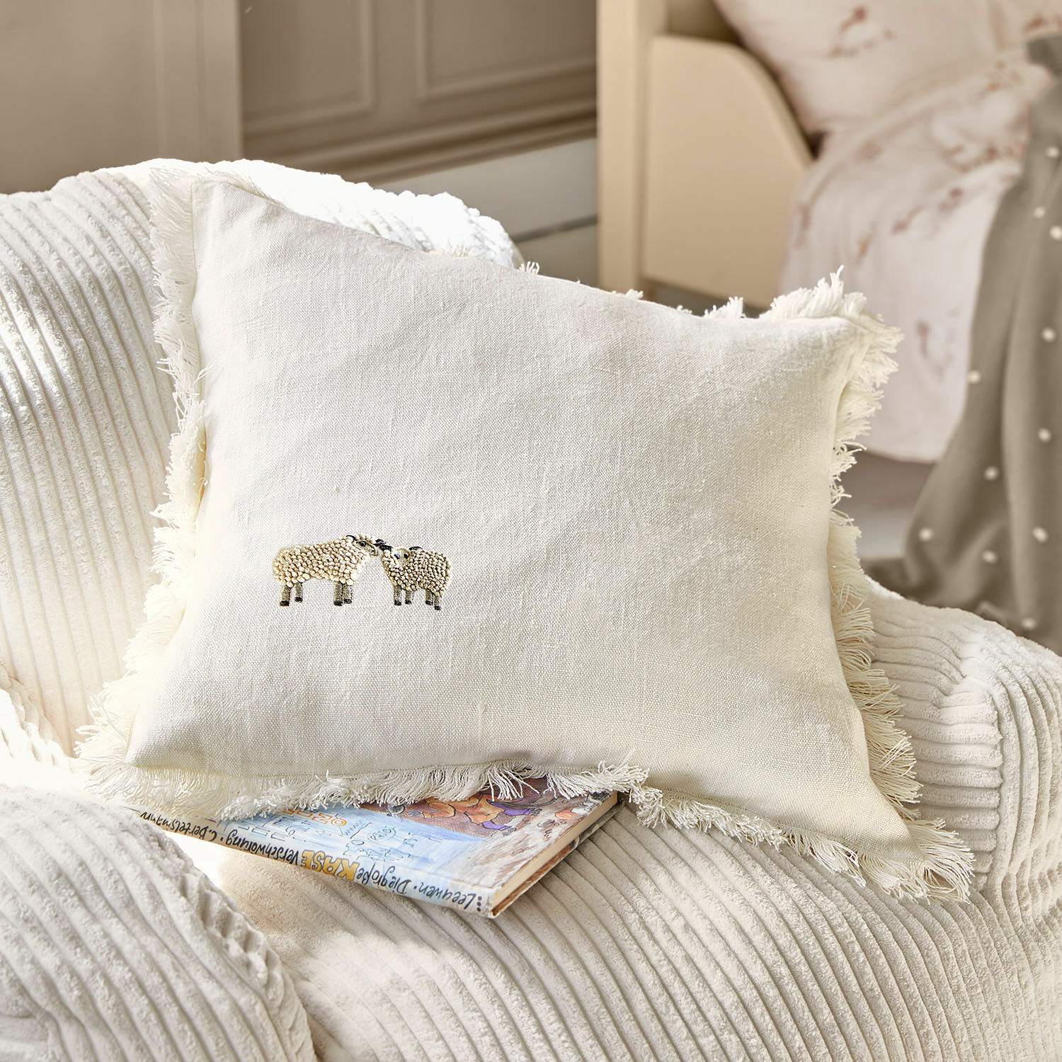 Kissenhülle Erianna Beige Leinenkissen mit Fransen und Schafstickerei auf weichem Sessel, Wohnaccessoire
