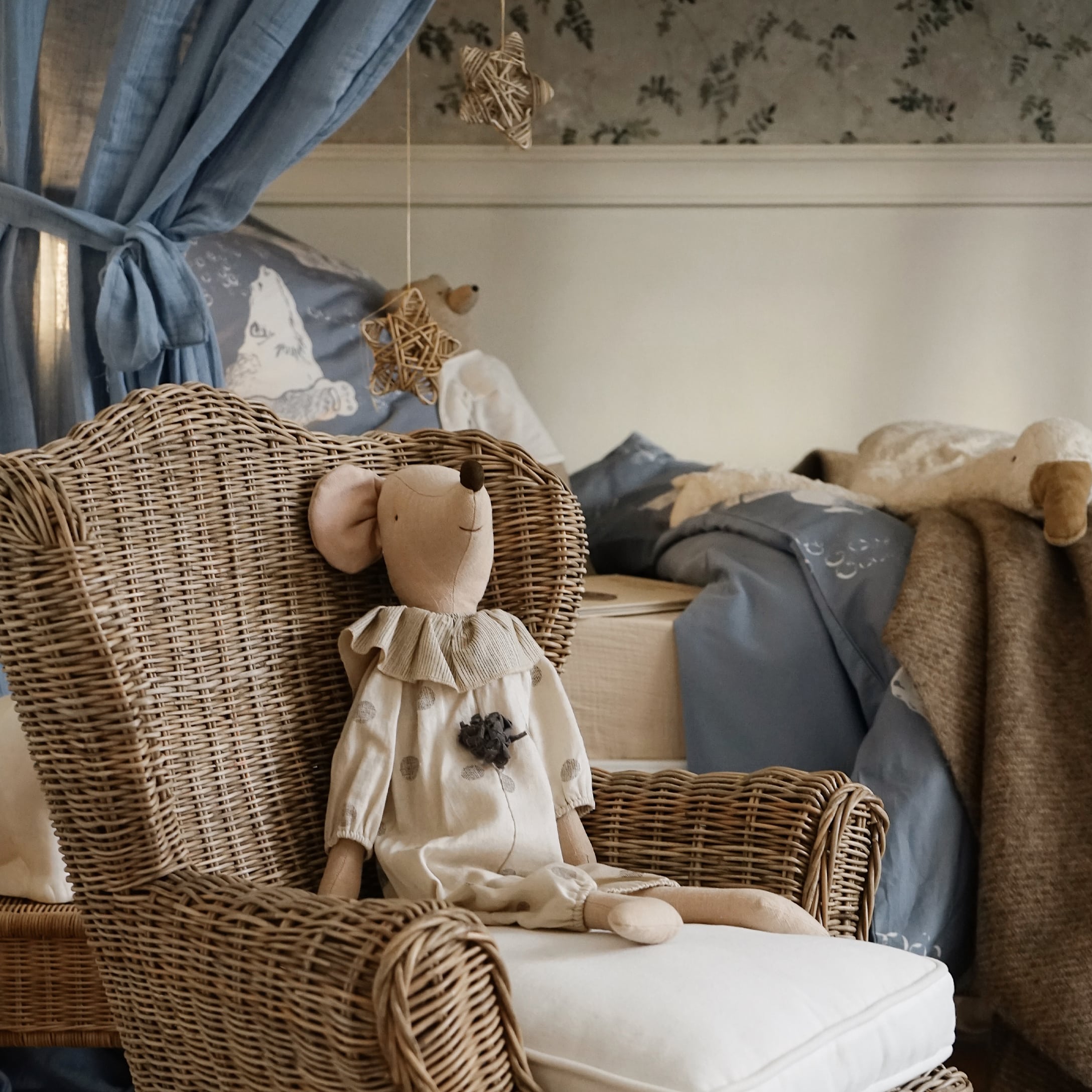 Natürlicher Rattansessel mit hellem Kissen und beiger Plüschmaus im Kinderzimmer