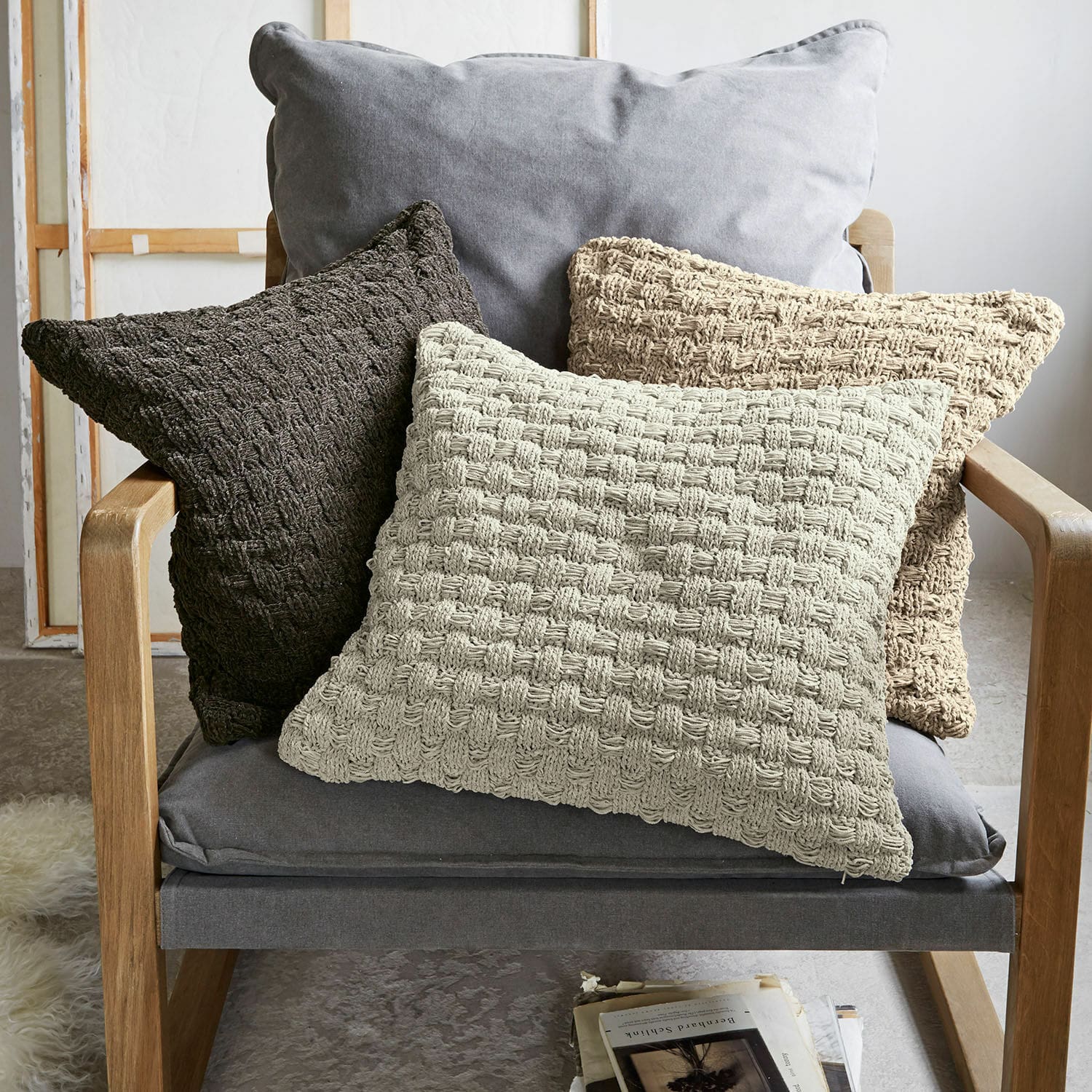 Kissenhülle 3er Set Antier Drei dekorative Kissen aus gewebtem Material in Beige- und Brauntönen auf grauem Sessel