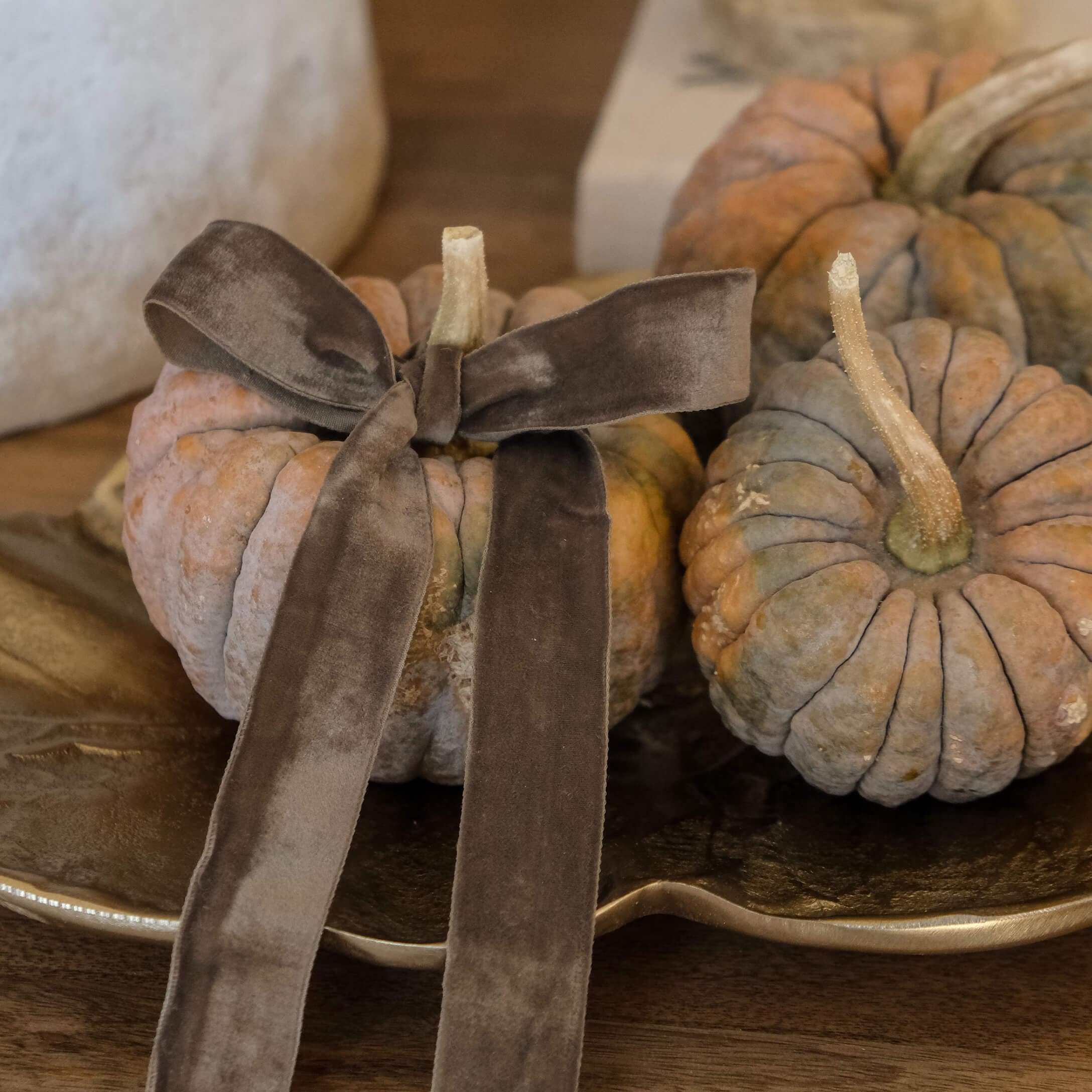 Dekorative orange-graue Kürbisse mit brauner Samtschleife auf goldener Platte auf Holztisch