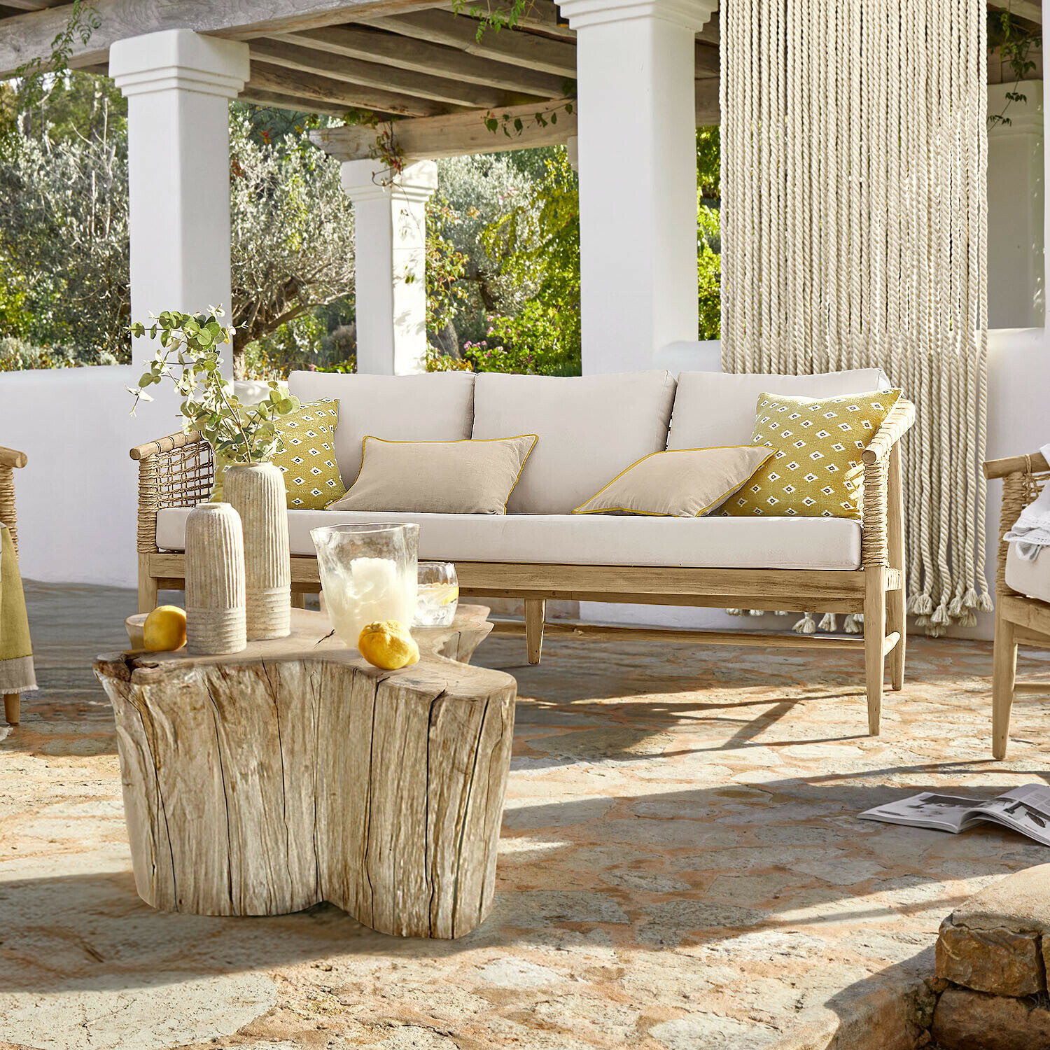 Sofa Roselva Hellholzsofa mit beigen Kissen und gelben Akzenten auf Terrasse mit Natursteinboden