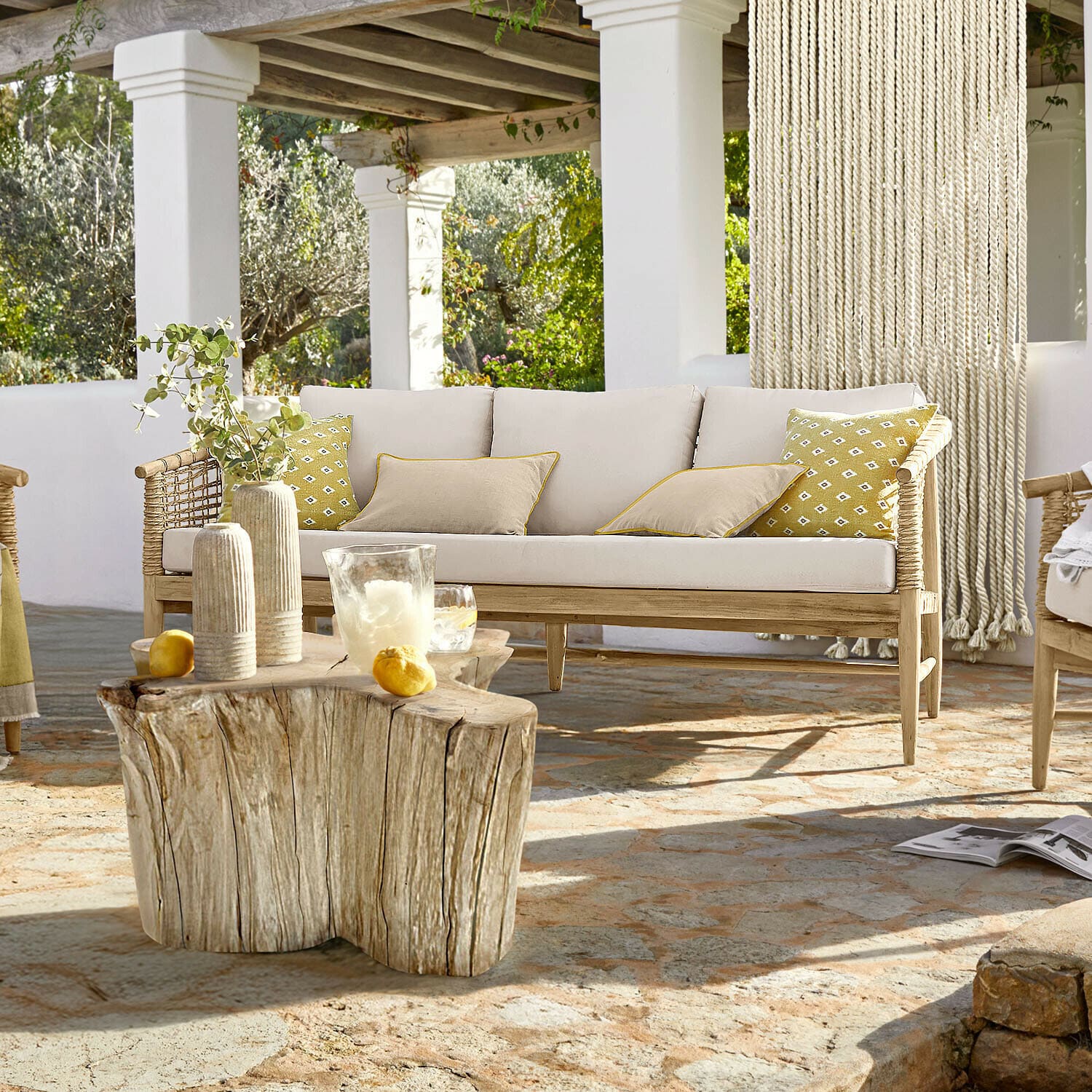 Sofa Roselva Hellholzsofa mit beigen Kissen und gelben Akzenten auf Terrasse mit Natursteinboden