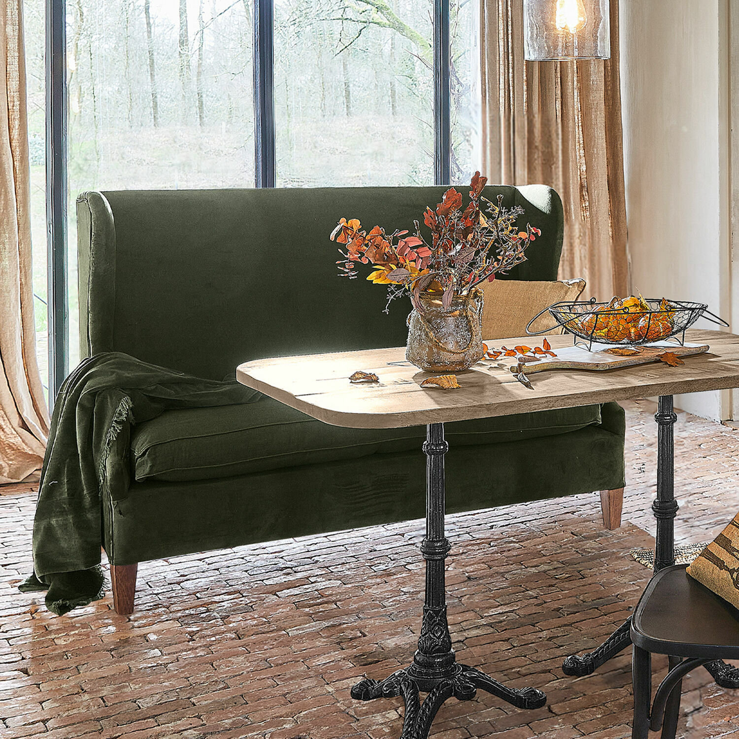 Sofa Ombra Grünes Samtsofa neben Holztisch mit Metallbeinen in hellem Raum mit Ziegelboden