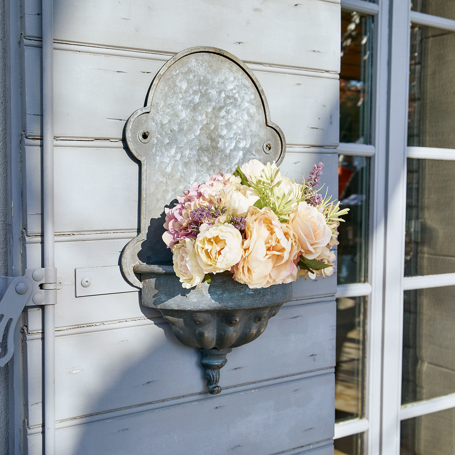 Pflanzbrunnen Millieur Metall-Wandblumenkasten mit pastellfarbenen Blumen an hellgrauer Außenwand