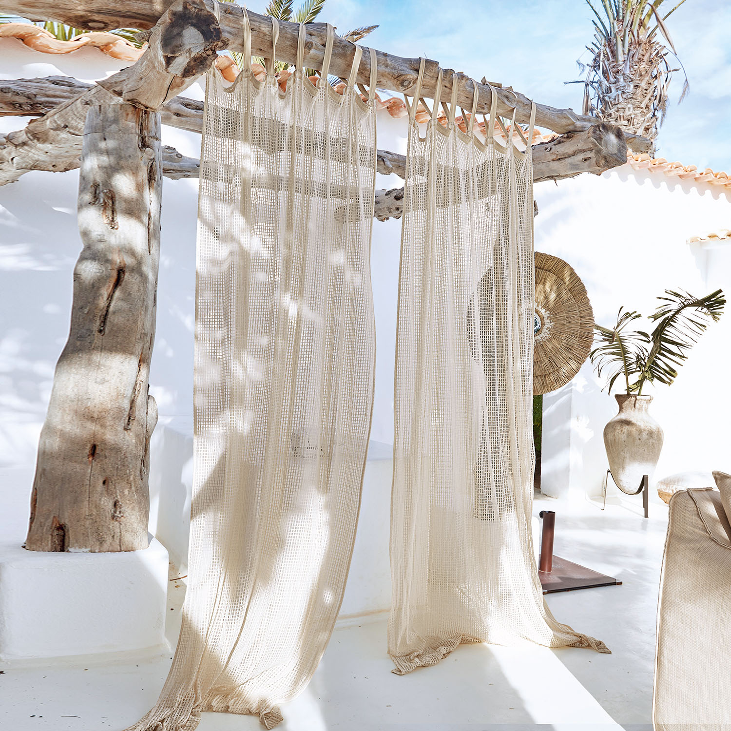 Beiger Netzvorhang mit Fransen an Holzkonstruktion in hellem mediterranem Ambiente