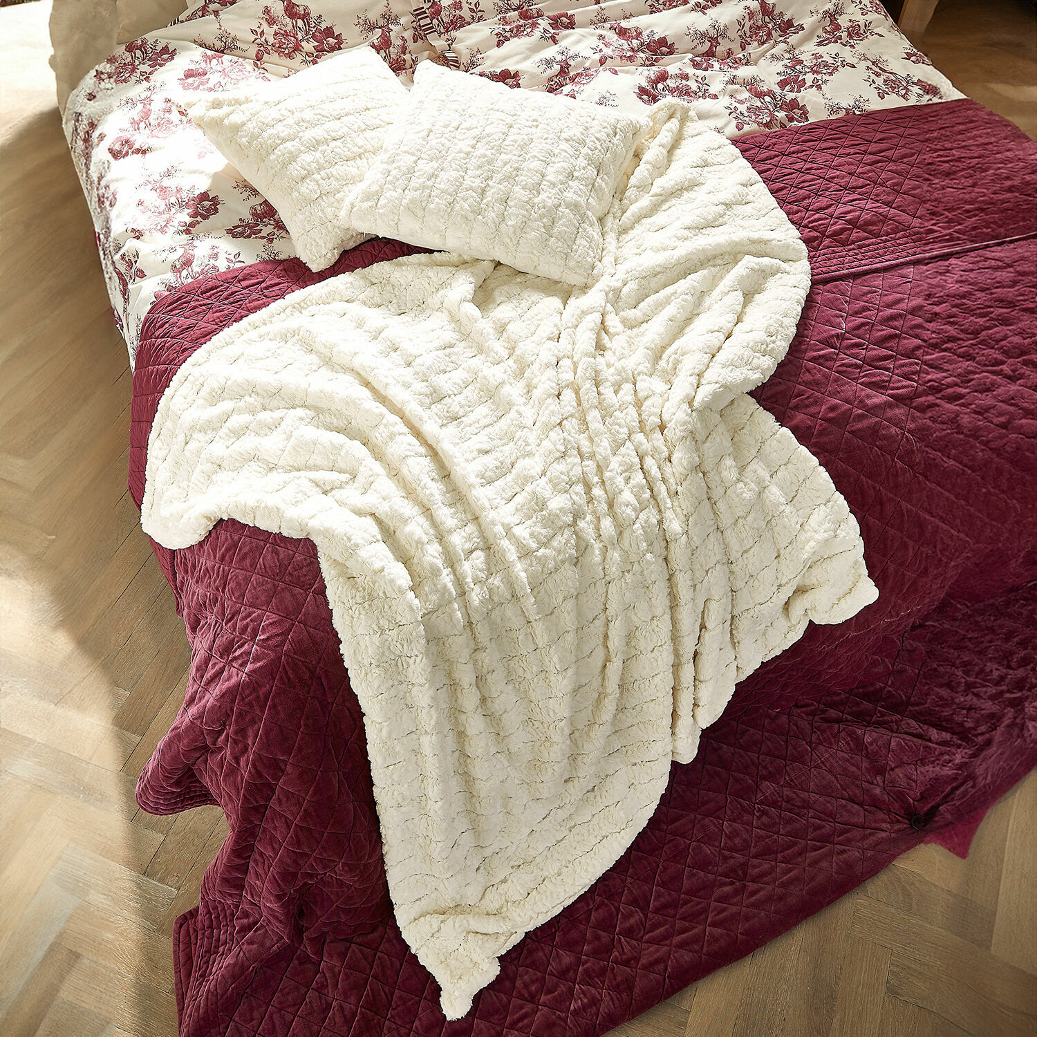 Plaid Dorelice Weiche cremefarbene Kuscheldecke und Kissen auf bordeauxroter Steppdecke auf dem Bett
