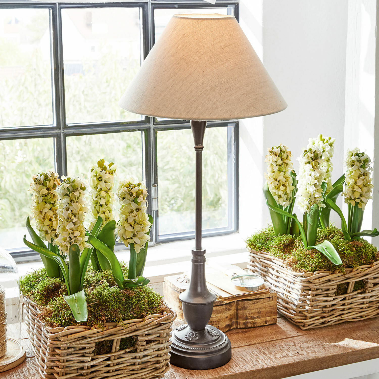 Tischlampe Barnwell Tischlampe mit Metallfuß und beigem Lampenschirm neben Weidenkörben mit weißen Blumen und Moos